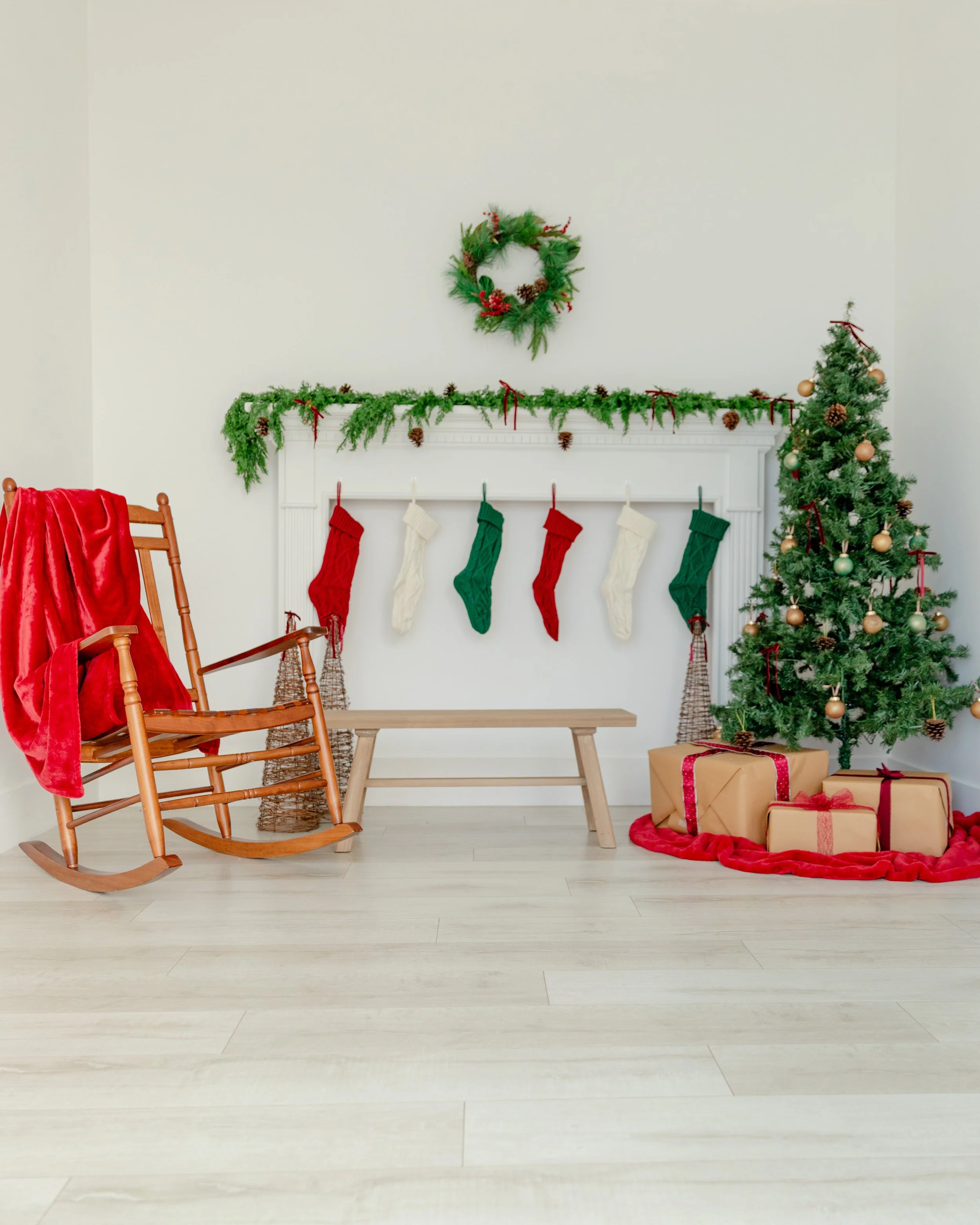 Celebrate the holidays in Studio C at Varsa Studios, American Fork, Utah. This inviting Christmas scene features a white fireplace adorned with lush garland, pinecones, and red ribbons, a classic tree with gold ornaments, and kraft-wrapped gifts rest