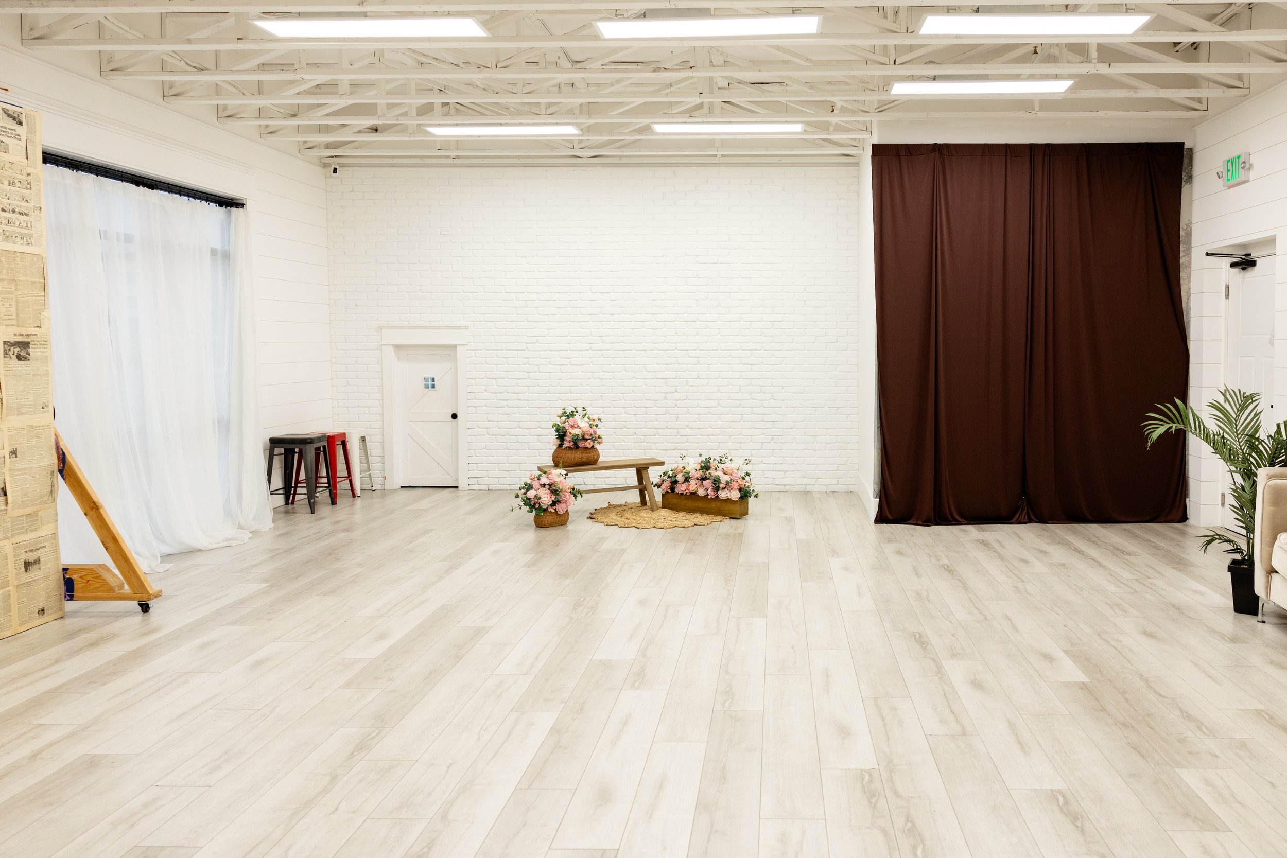 A bright open studio with benches and a fabric draped bed, sheer curtains, and ample room for photoshoots.