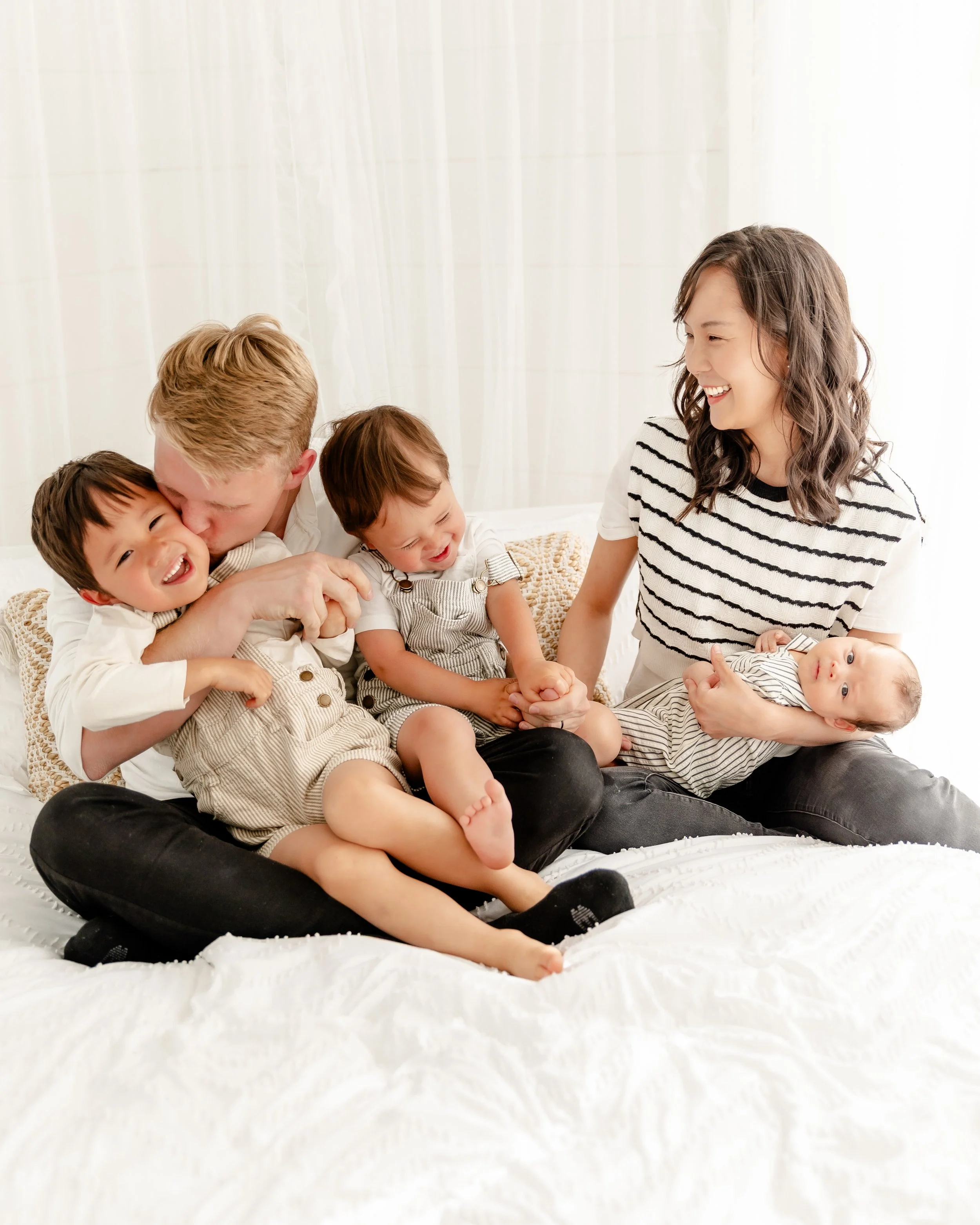 Candid family photos on a white bed in a bright natural light Utah photography studio, ideal for lifestyle and in-home-style sessions.