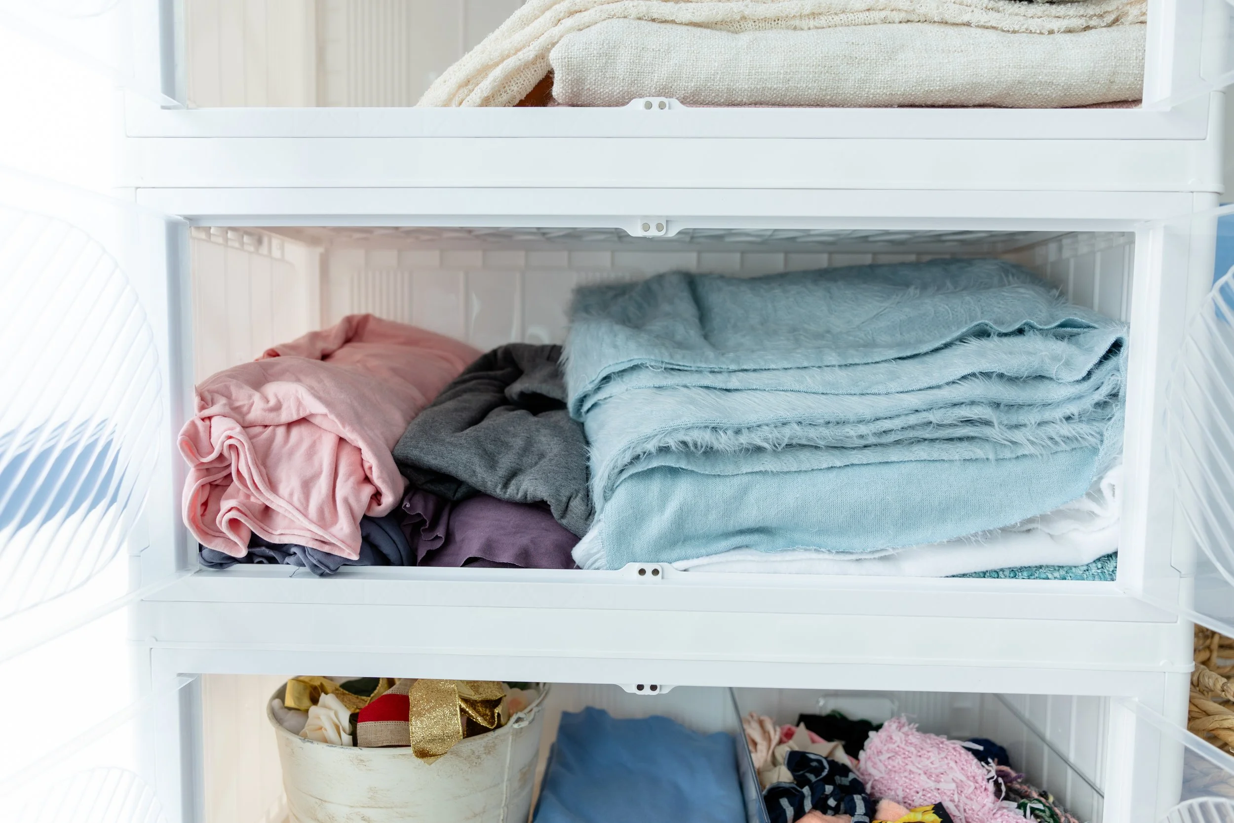 Neatly folded newborn photography wraps and blankets in soft pink, gray, blue, and neutral tones organized inside Studio C at Blank Space American Fork.