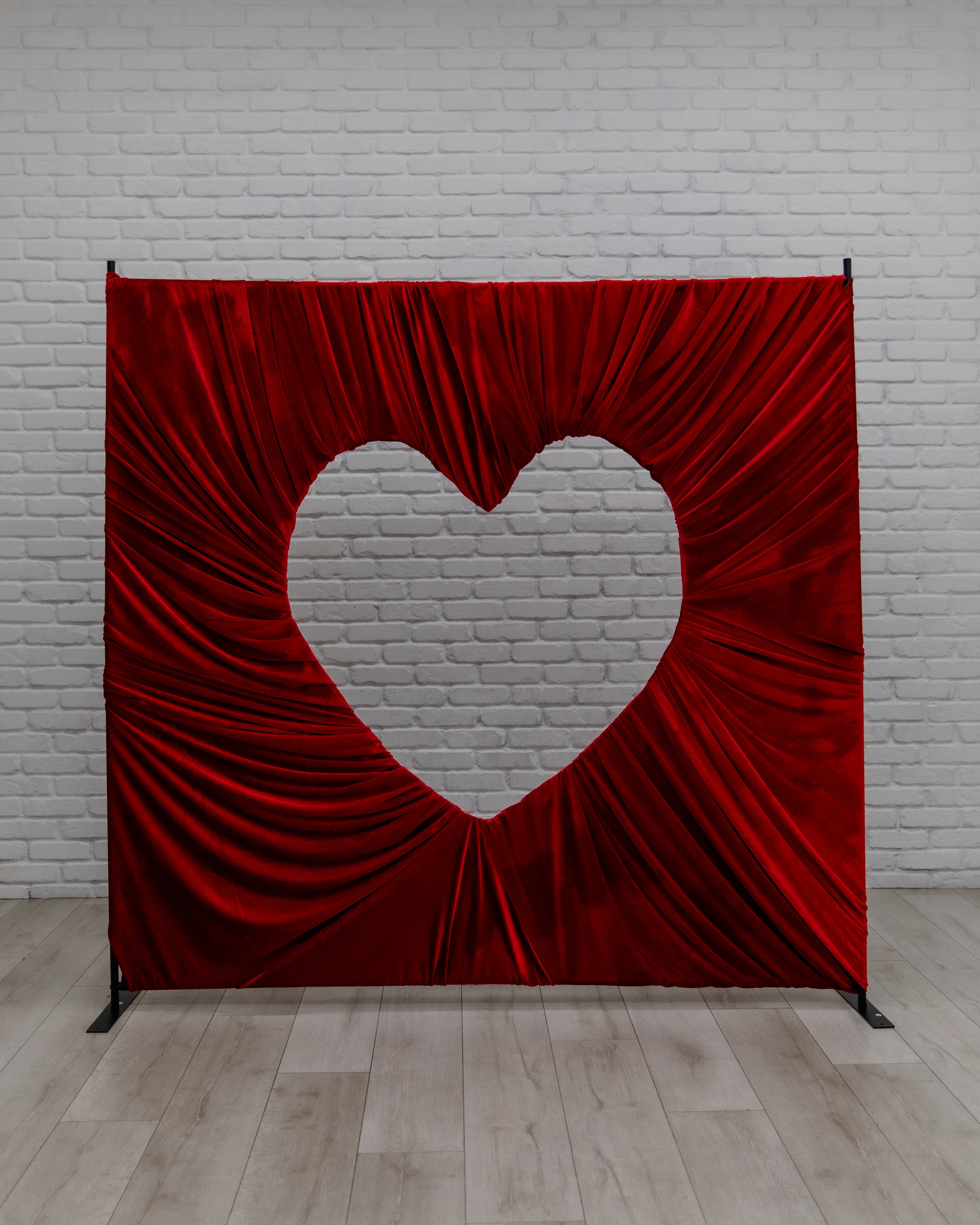 Red fabric heart cutout backdrop against a white brick wall in Studio B at Varsa Studios American Fork, a bold Valentine’s Day photo setup for photographers, engagements, couples sessions, and content creators.