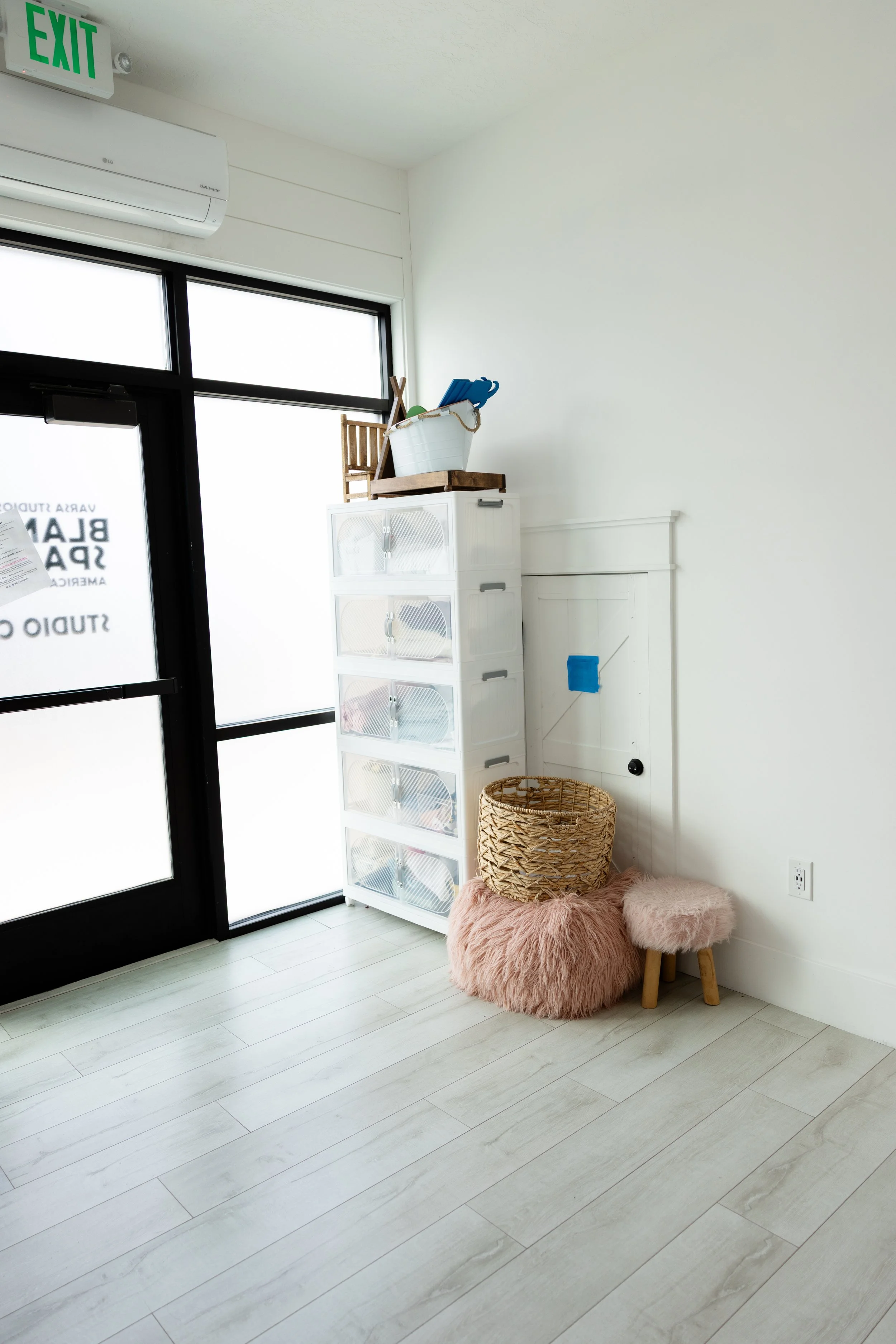 Corner of Studio C at Blank Space in American Fork, Utah showing organized newborn prop storage, baskets, stools, and bright natural light from large windows.