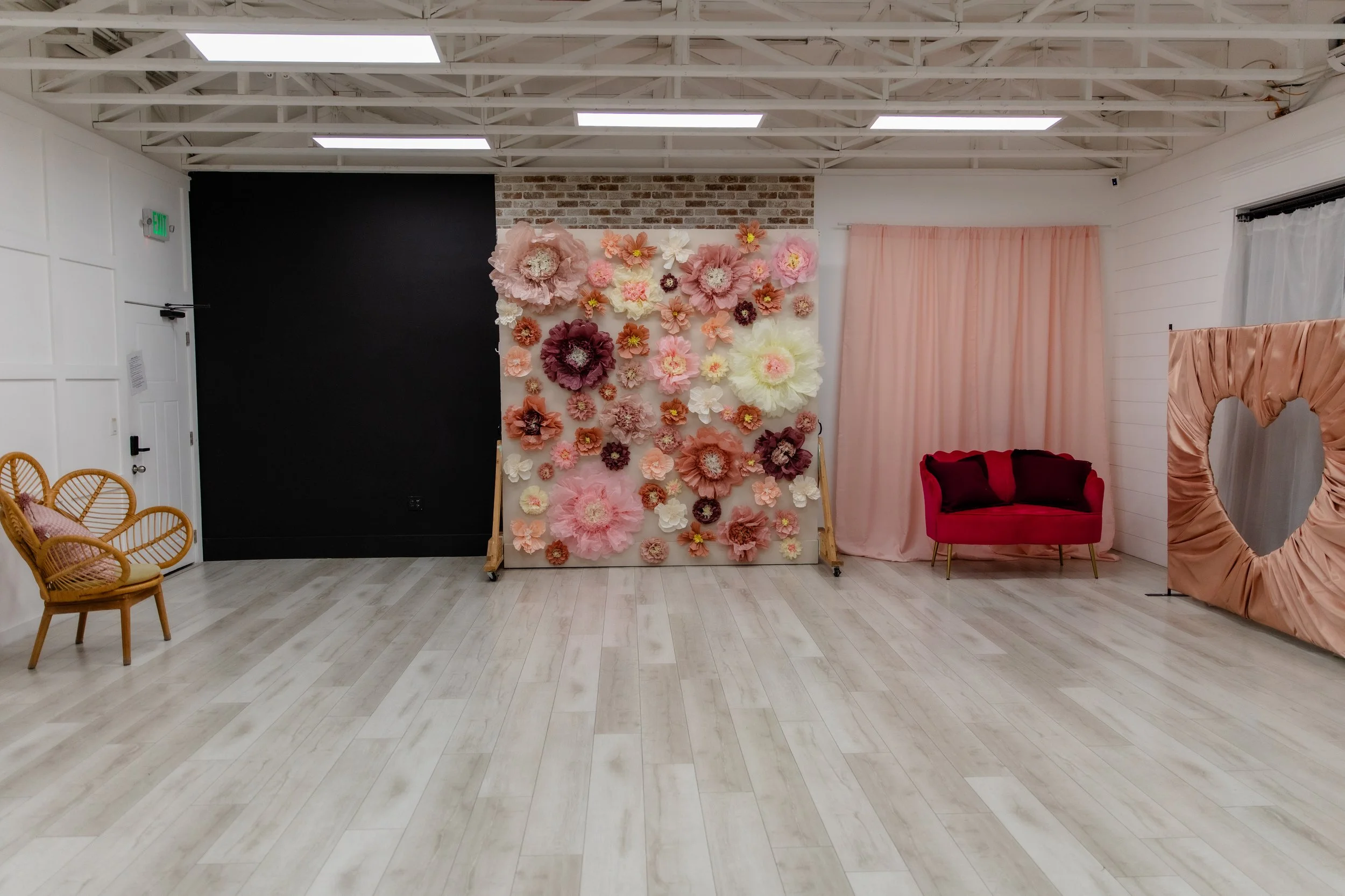 A large bright room with various fabric and brick backdrops, two couches, potted plants, and large windows with lots of natural light