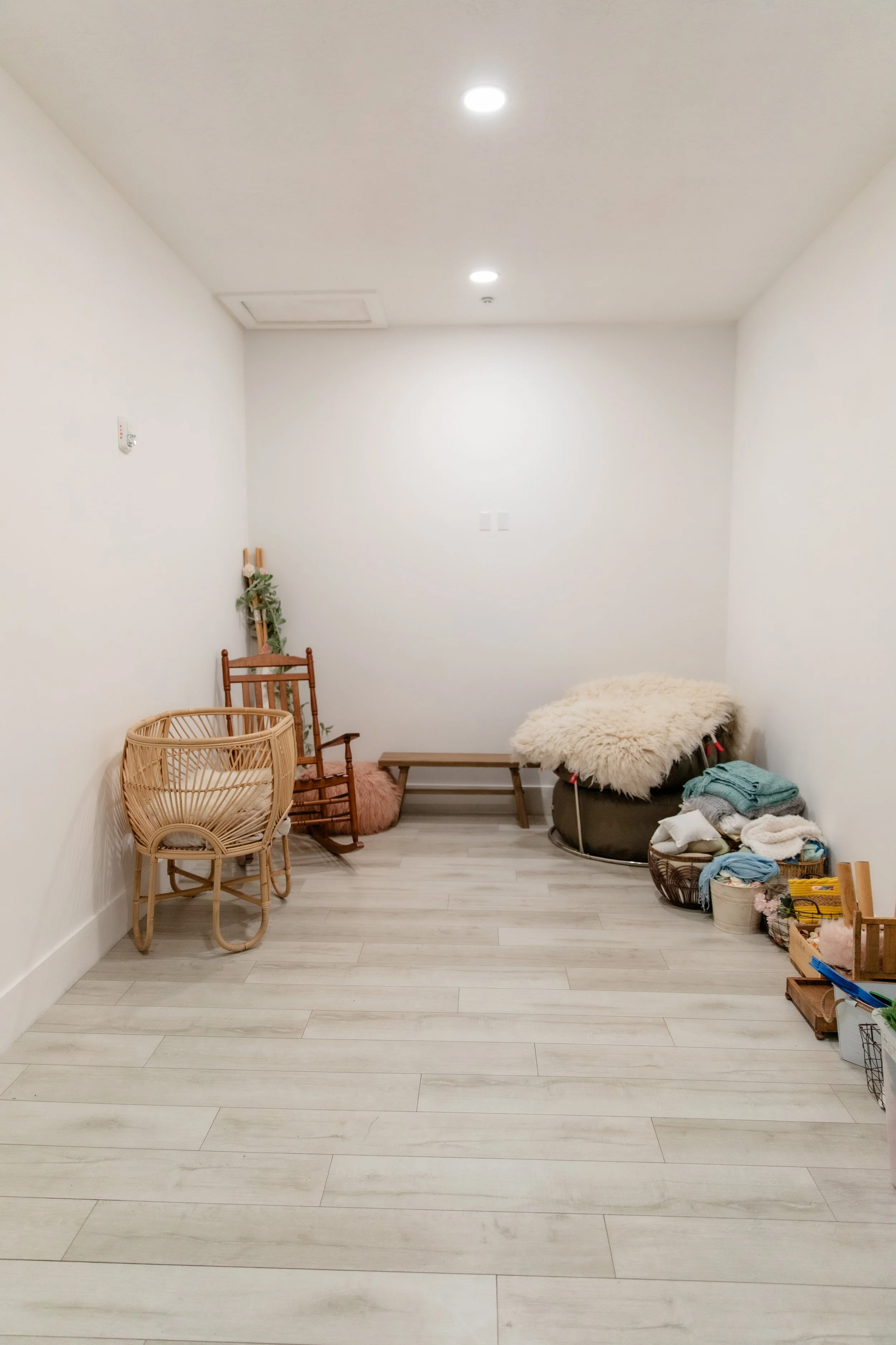 Cozy Christmas photo setup in Studio C featuring a classic rocking chair with a red blanket, a bench framed by a festive faux mantel with stockings, and a decorated Christmas tree with gold and green ornaments, gifts, and garland accents.