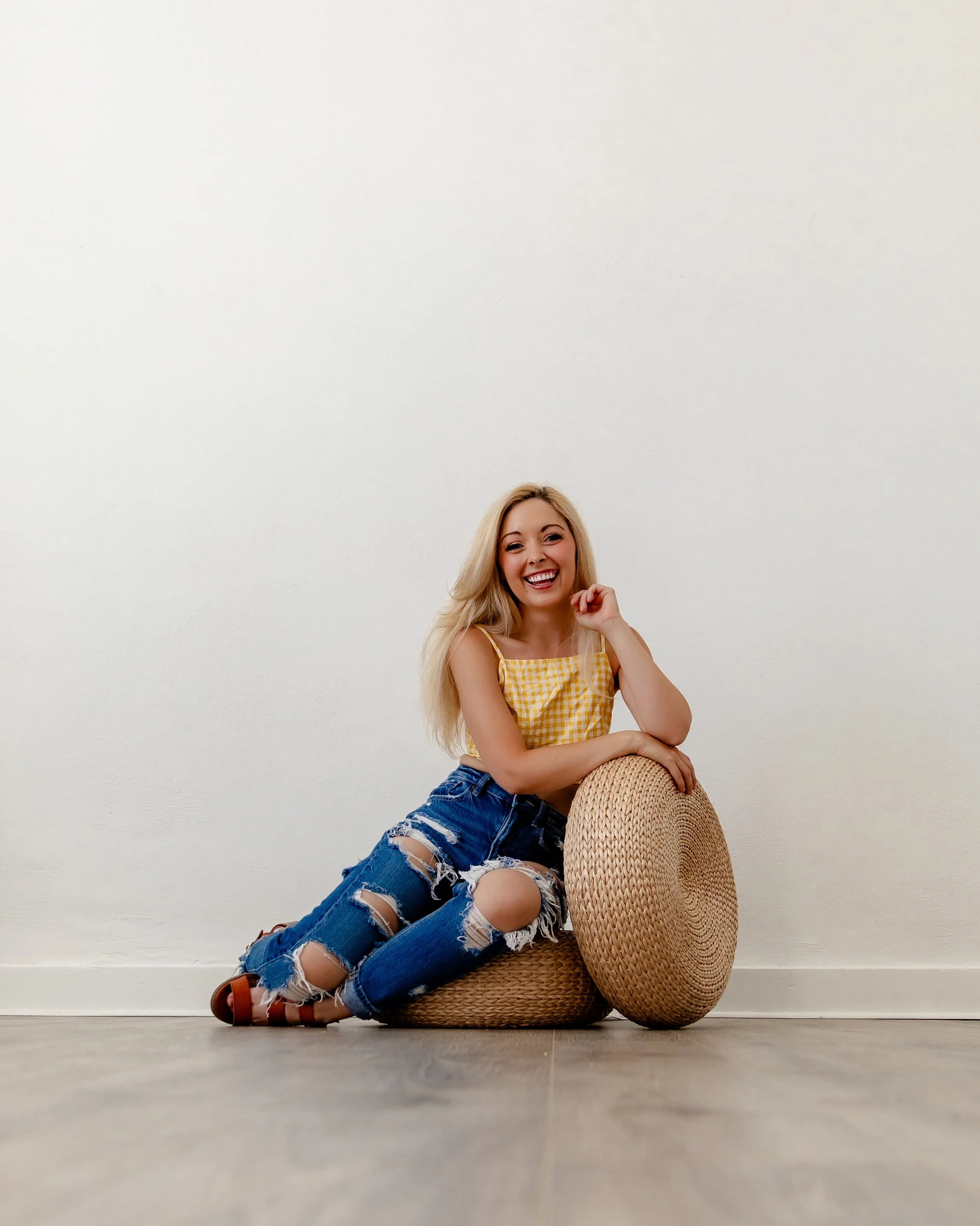 Smiling woman posing in Alcove Studio, Springville Utah, leaning on a pouf in natural light