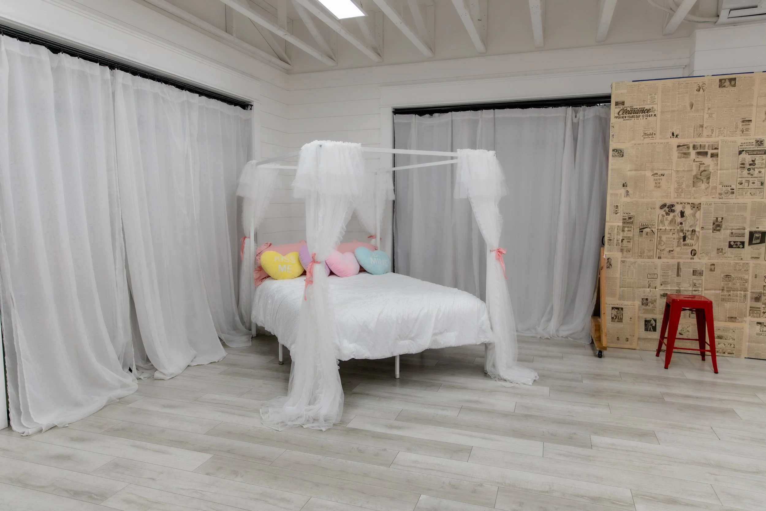 White canopy bed with sheer curtains and pastel heart pillows in Studio B at Varsa Studios American Fork, a Valentine’s Day themed setup for photographers, couples sessions, boudoir photography, and lifestyle content creation.