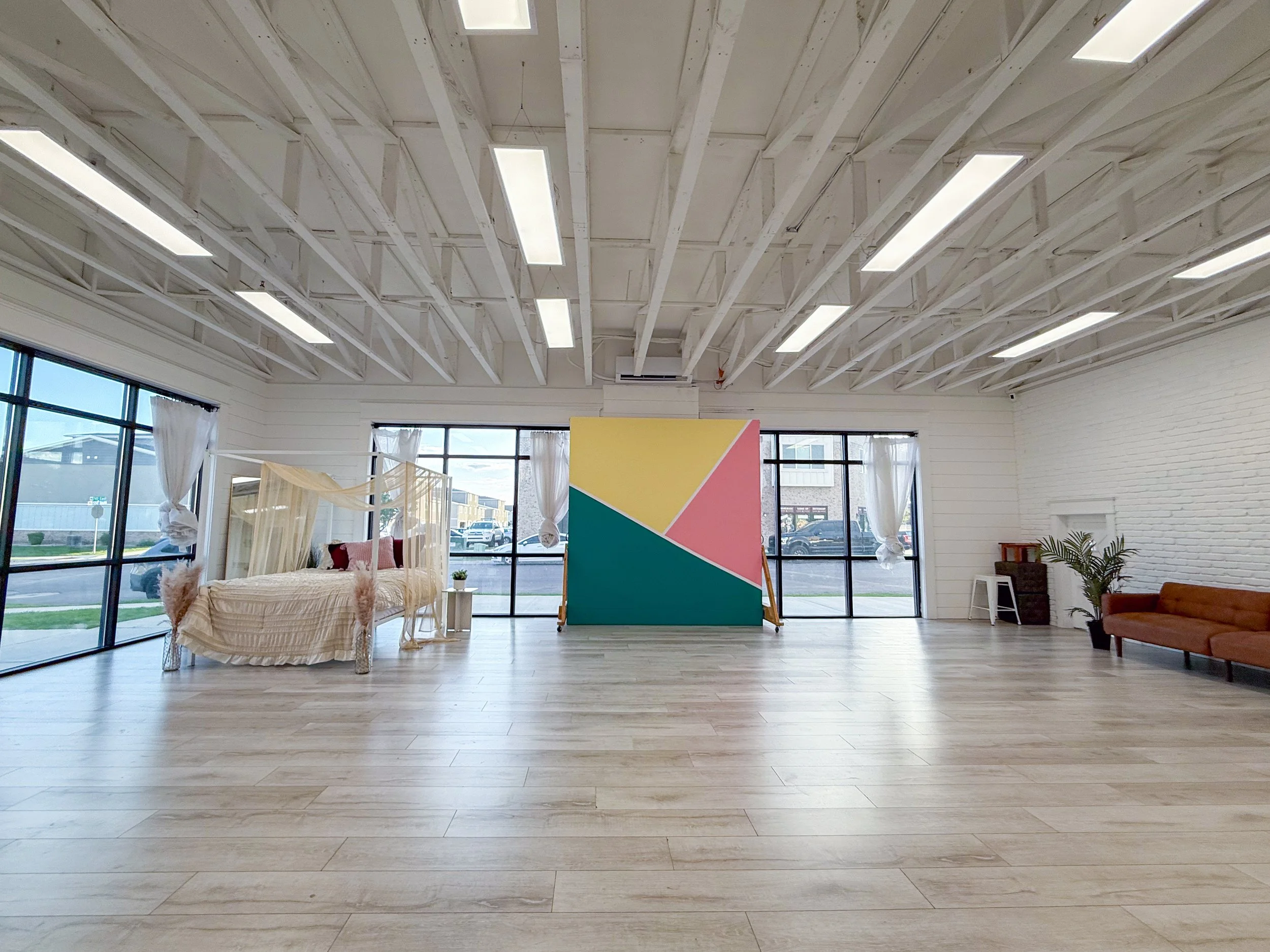 Blank Space Studio B is a large natural light photography studio and content creation space located in American Fork, Utah. Featuring floor-to-ceiling windows, movable feature walls, lifestyle furniture, a canopy bed, white brick wall, colorful geome