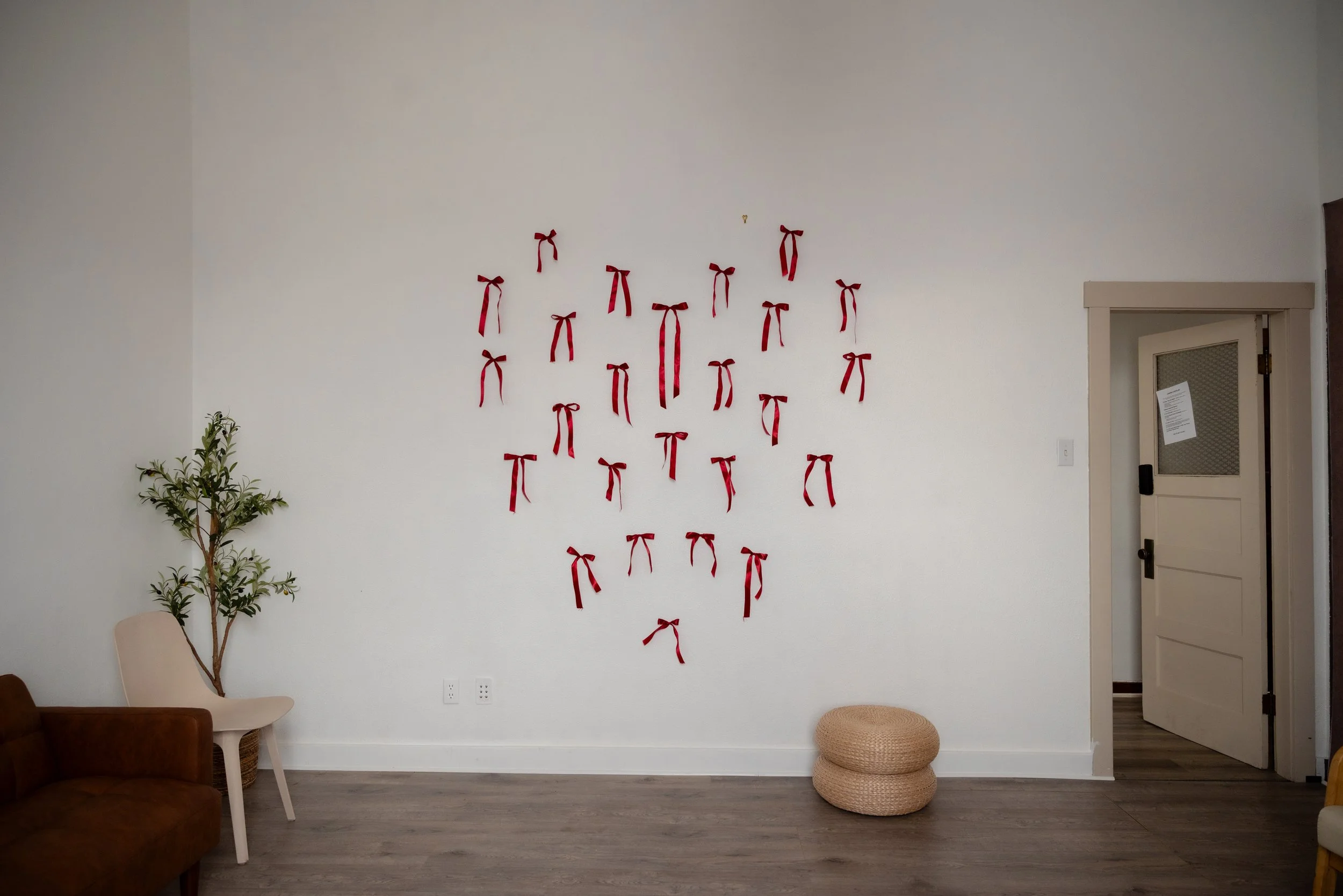 Minimalist white studio wall in The Alcove studio in Springville, Utah, decorated with red ribbon bows for seasonal Valentine’s photography sessions.