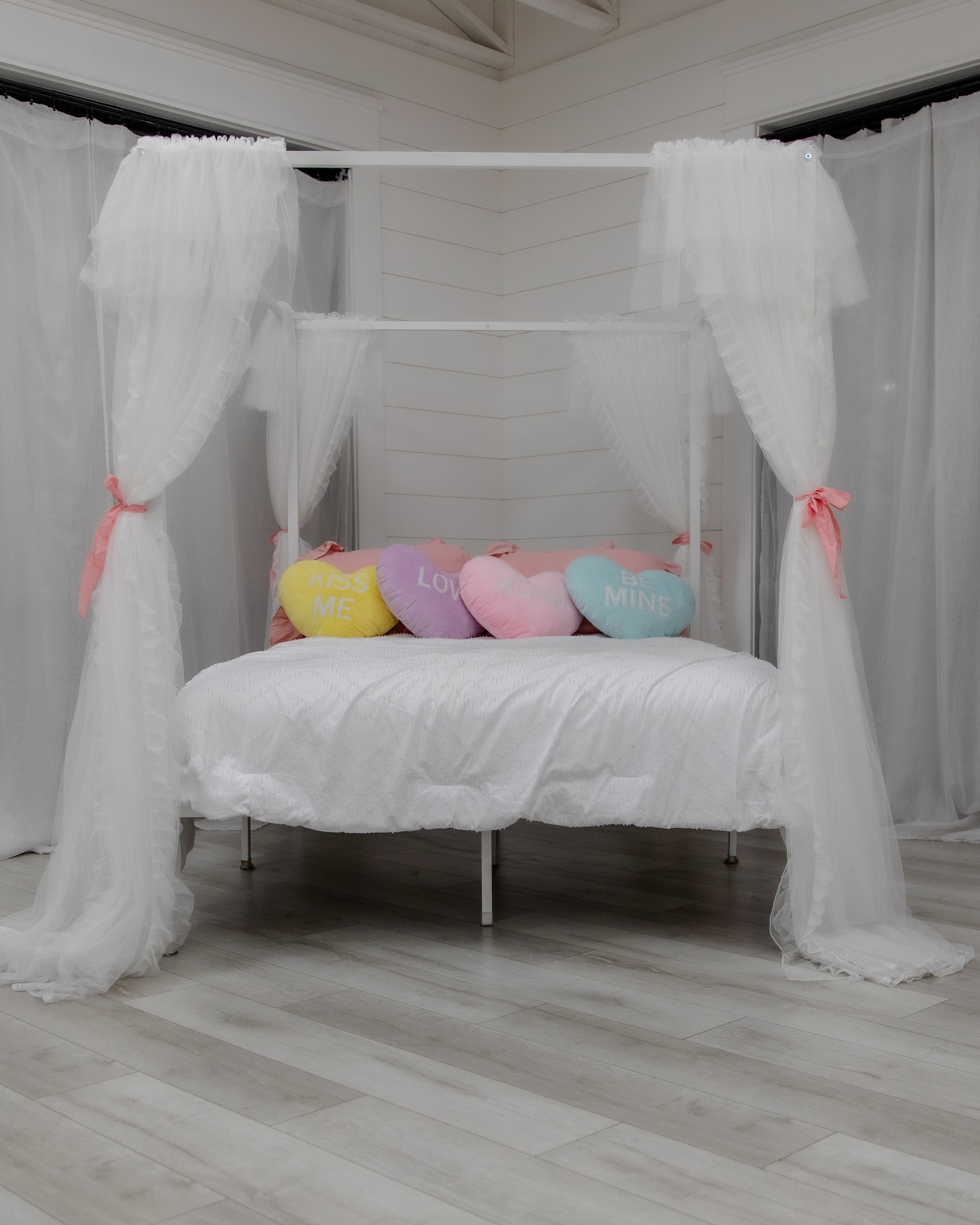 White canopy bed with sheer curtains and pastel heart pillows in Studio B at Varsa Studios American Fork, a Valentine’s Day themed setup for photographers, couples sessions, boudoir photography, and lifestyle content creation.