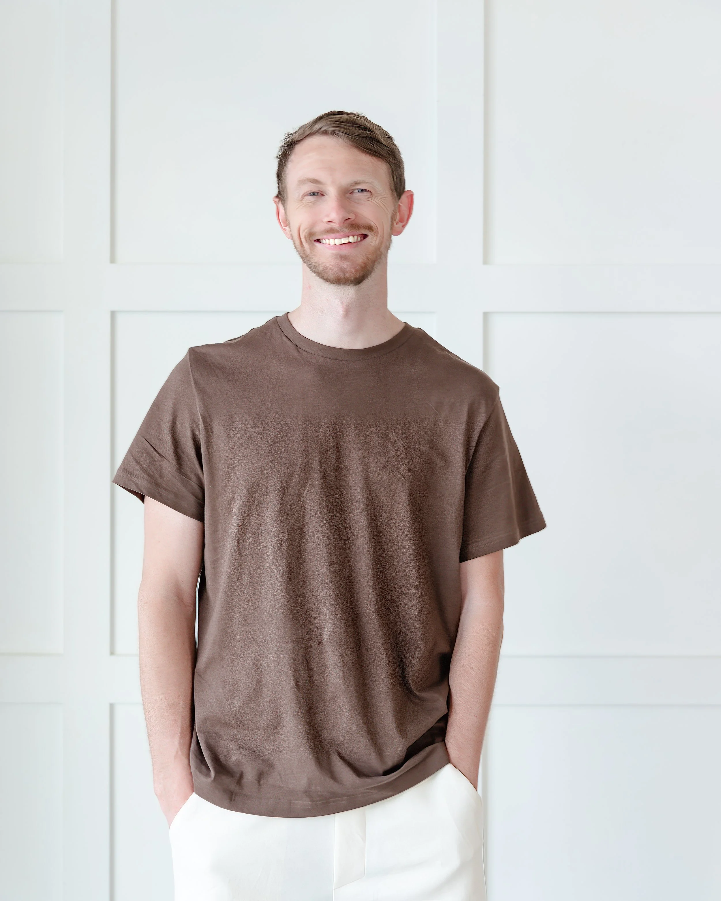 Portrait of a man in bright studio with a white wooden accent wall backdrop.