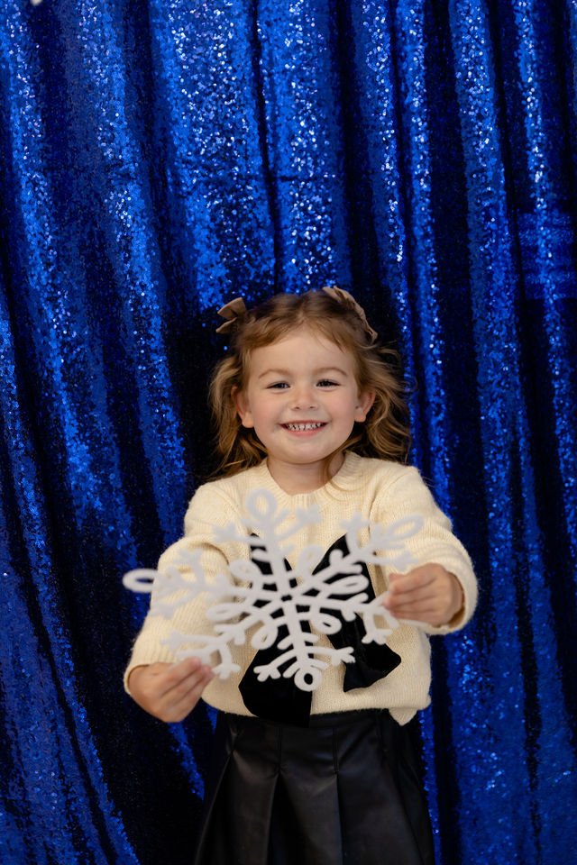 Playful children’s Christmas photo captured in Studio A at Varsa Studios, featuring a sparkling blue sequin backdrop and oversized snowflake prop. Perfect for holiday portraits with a pop of fun and color.