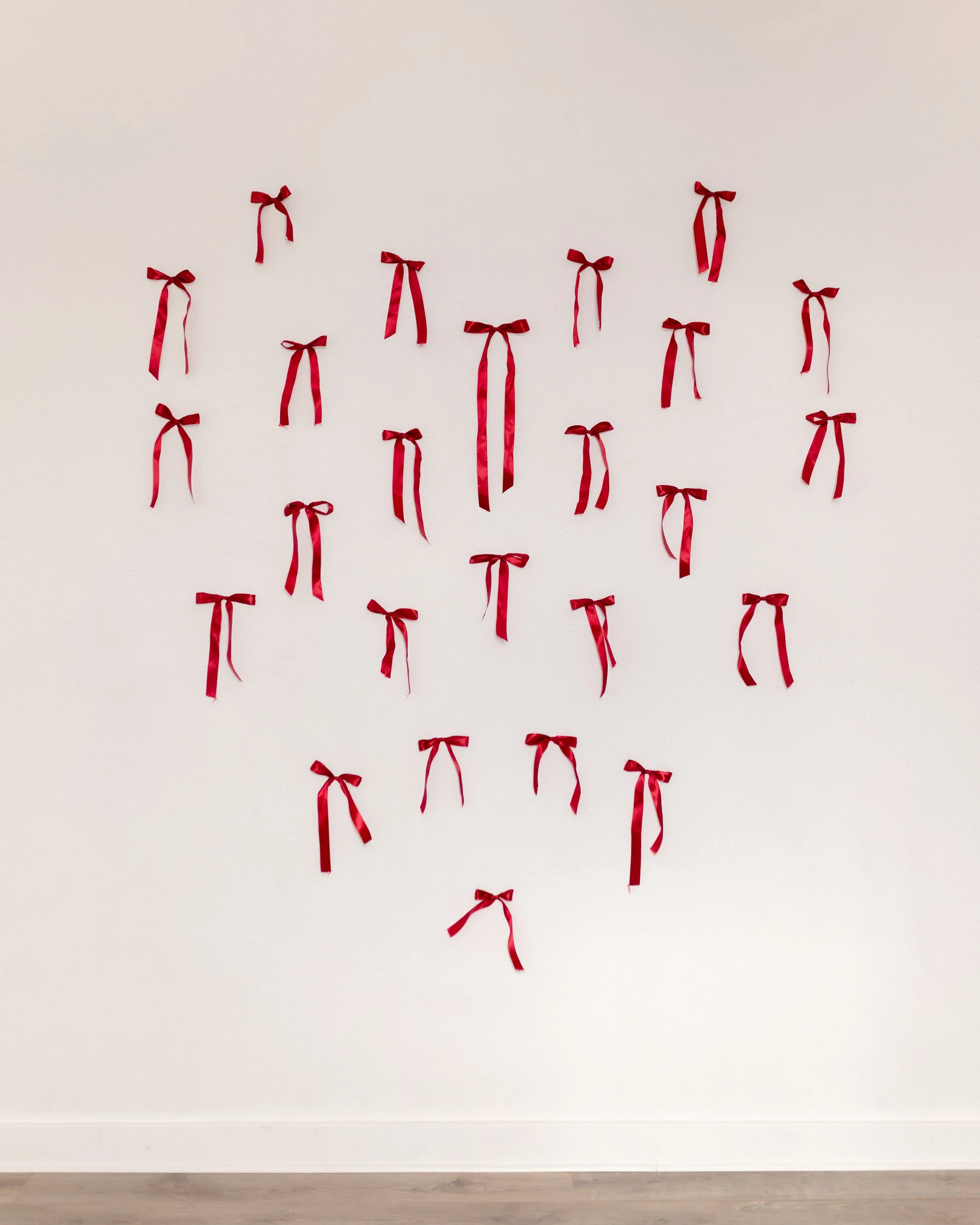 White wall in The Alcove natural light photography studio in Springville, Utah, styled with red satin ribbon bows for Valentine’s Day photo sessions.