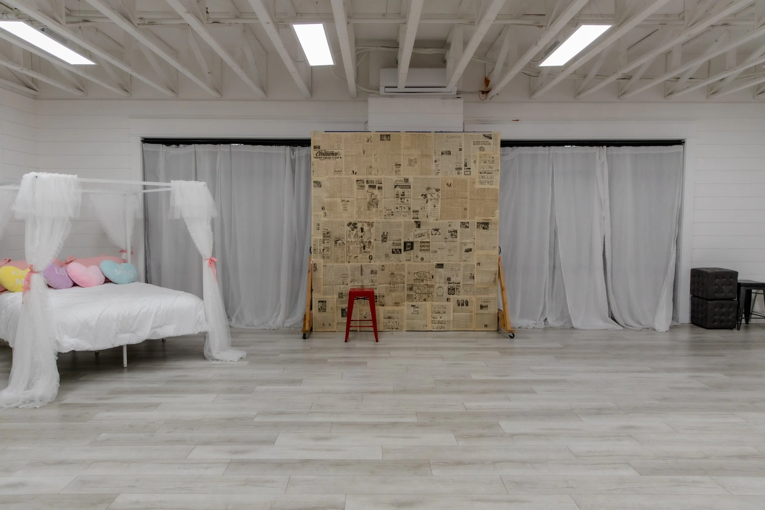 A bright open studio with benches and a fabric draped bed, sheer curtains, and ample room for photoshoots.