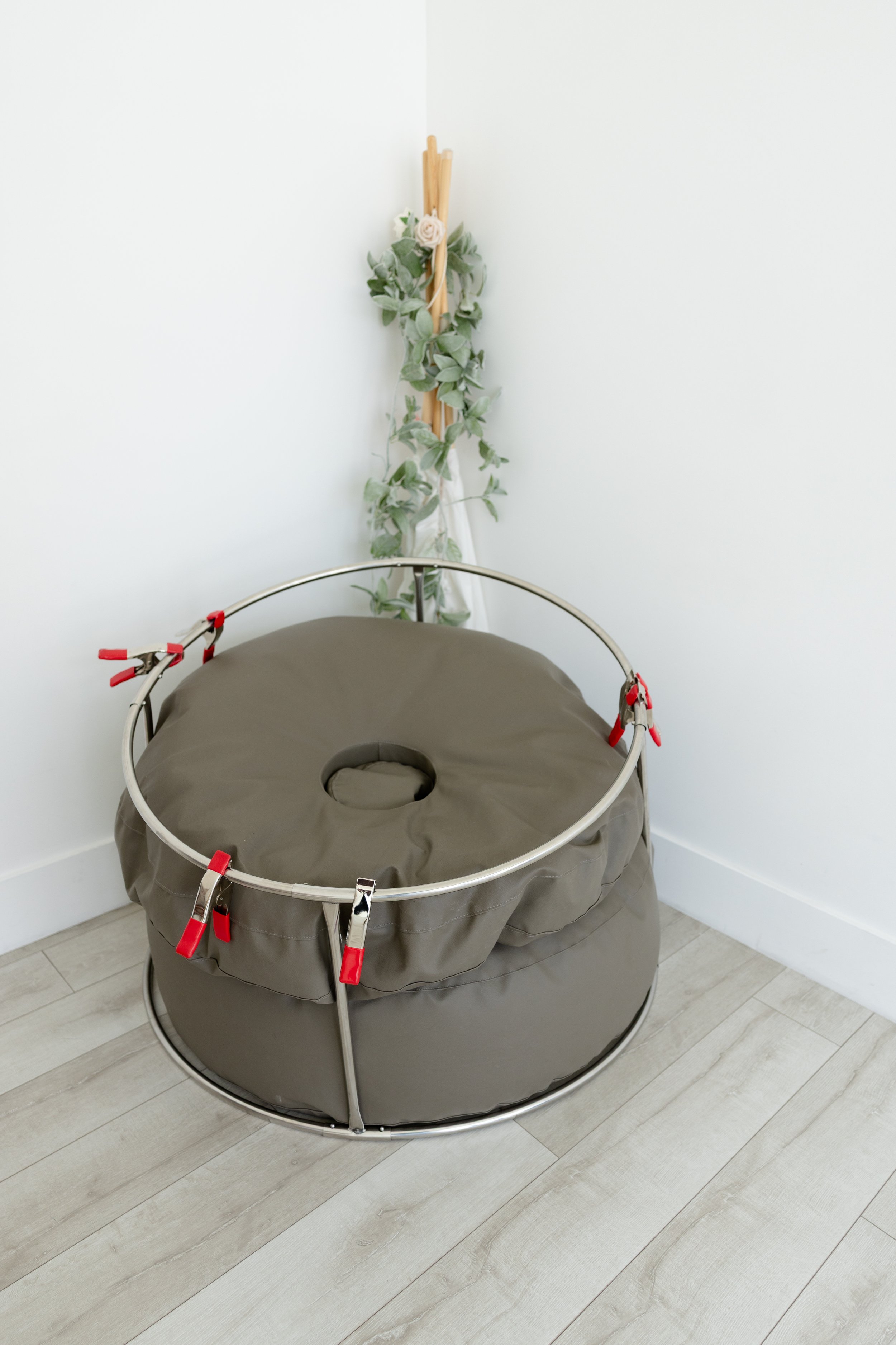 Newborn photography posing bean bag with neutral gray fabric and support frame in Studio C at Blank Space American Fork, styled against a clean white wall with soft greenery accents.