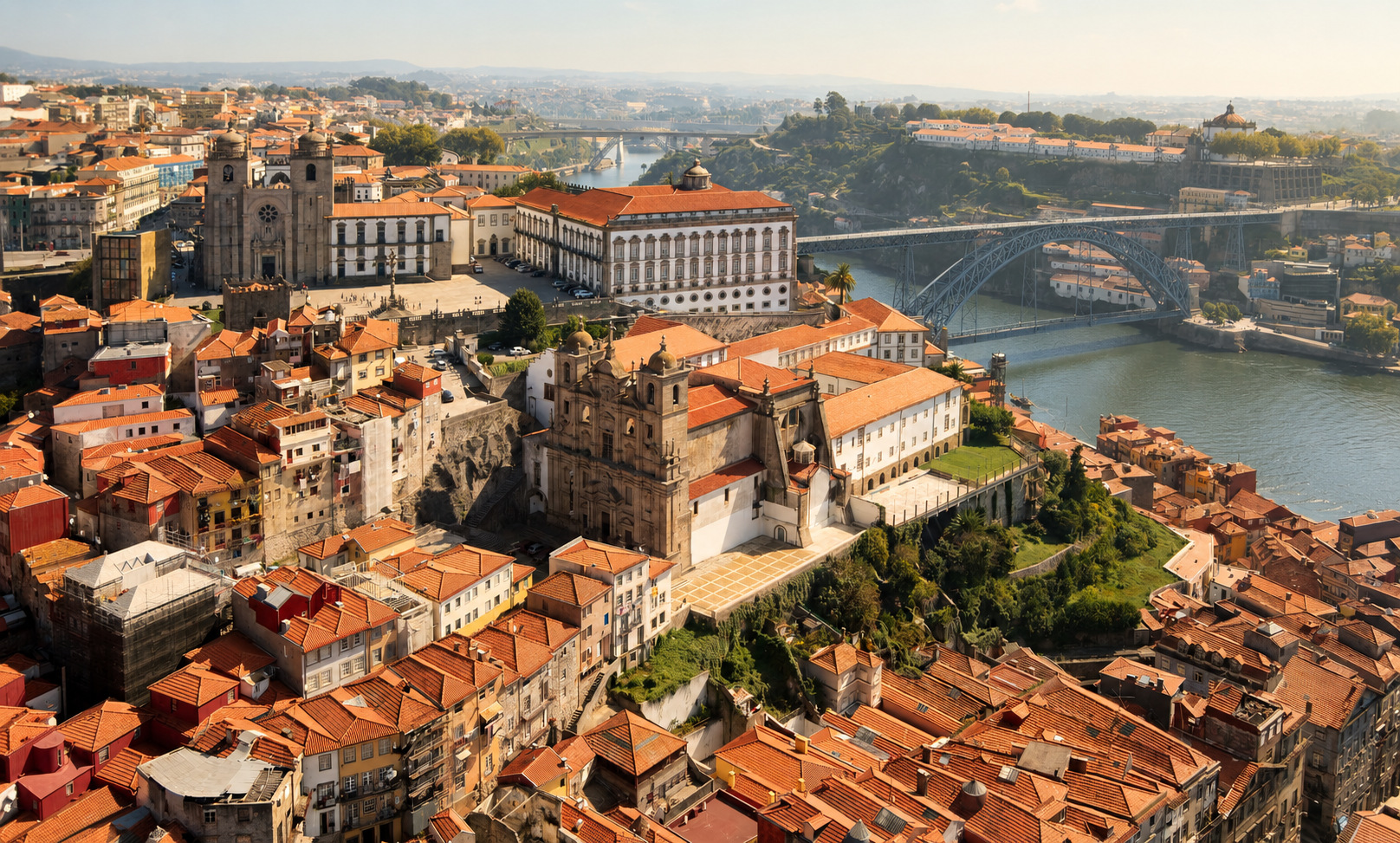 Historic center of Porto, Portugal, with Porto Cathedral, terracotta rooftops, hillside architecture, and the Douro River in the distance.