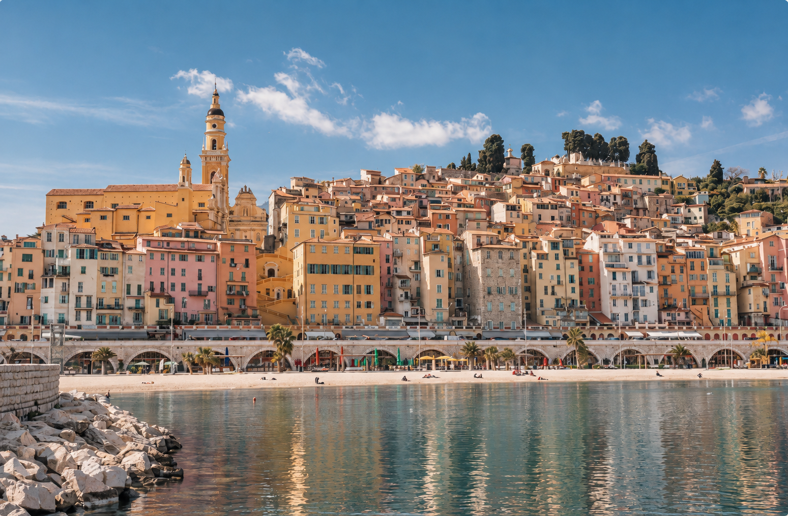 Colorful hillside buildings and the historic basilica of Menton, France, overlooking the Mediterranean waterfront on the French Riviera.