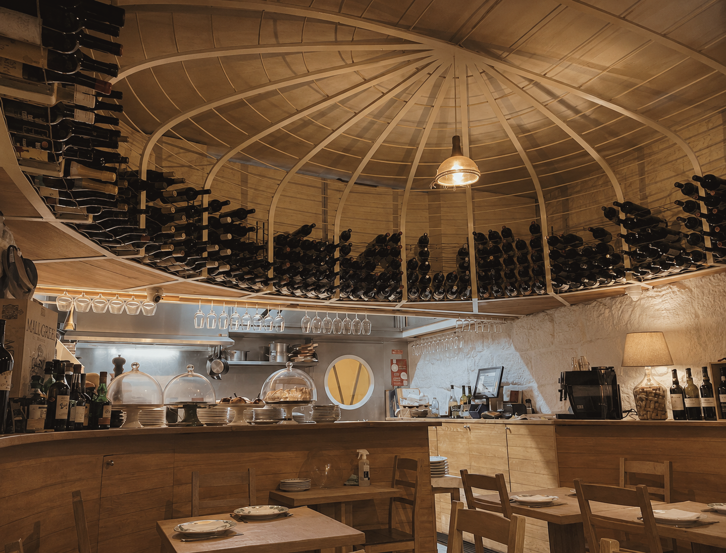 Taberna dos Mercadores restaurant in Porto, Portugal, featuring an intimate rustic dining room with wood interiors, open kitchen, and wine bottles displayed overhead.