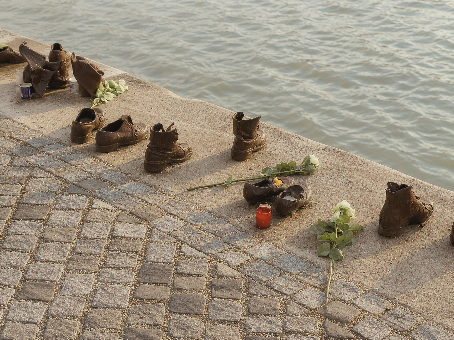 Shoes on the Danube Bank memorial in Budapest, Hungary, with the Hungarian Parliament Building and Danube River nearby.