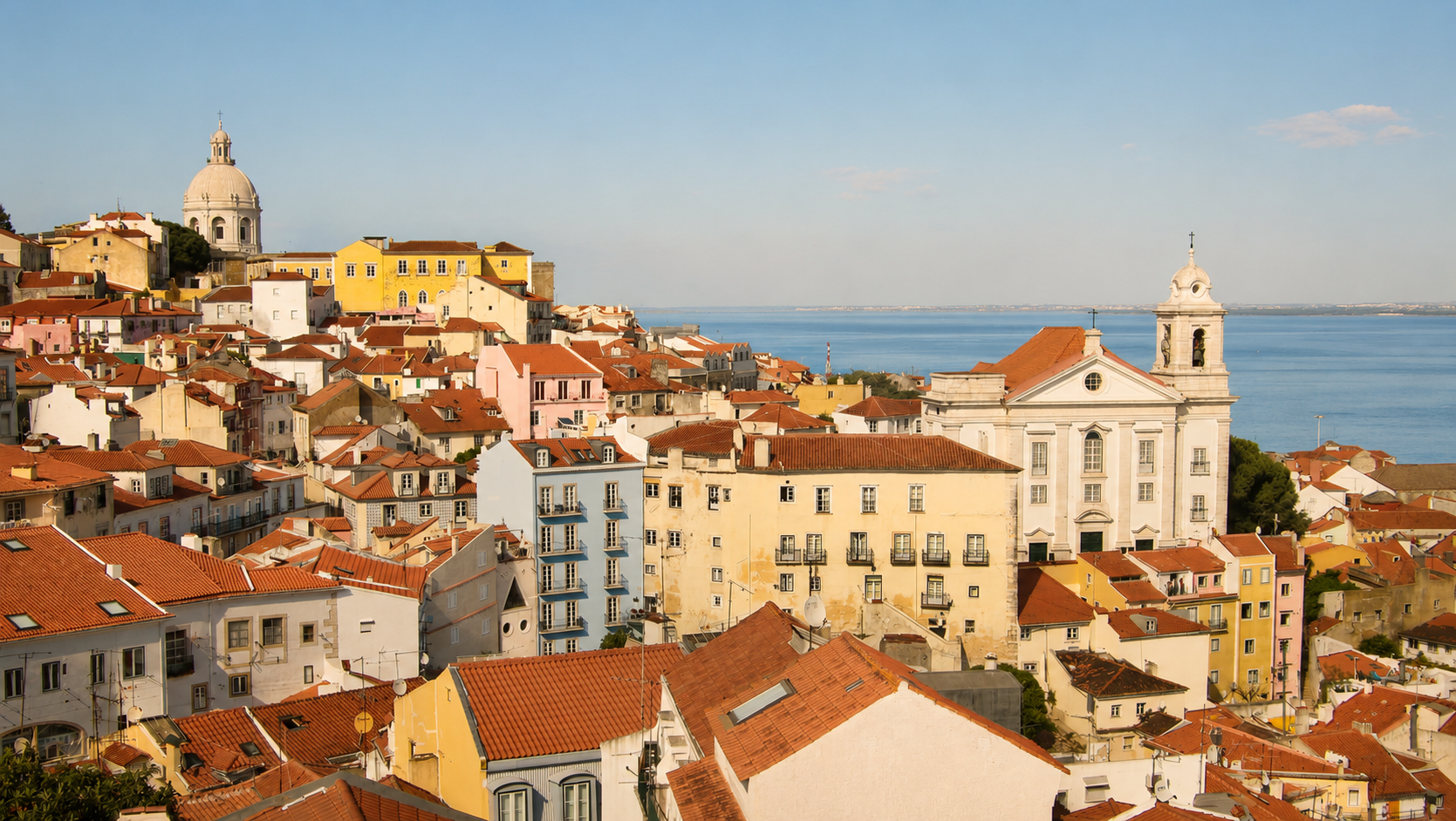 Historic Alfama district in Lisbon, Portugal, with colorful hillside buildings, terracotta rooftops, and the National Pantheon overlooking the Tagus River.