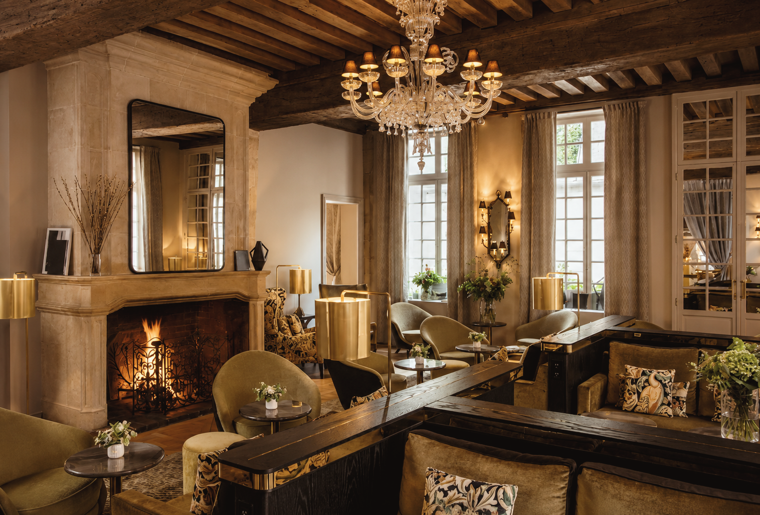 Elegant lounge at Hôtel d’Aubusson in Paris, France, featuring a grand crystal chandelier, wood-beamed ceilings, a glowing fireplace, and refined historic furnishings.