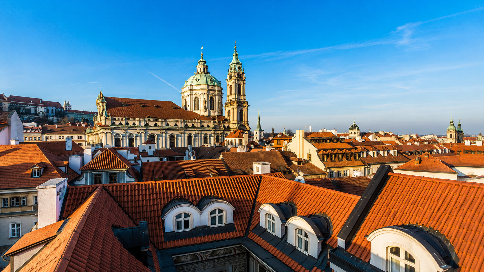 St. Nicholas Church in Malá Strana, Prague, Czech Republic, rising above historic red-tiled rooftops with its Baroque dome and bell tower.
