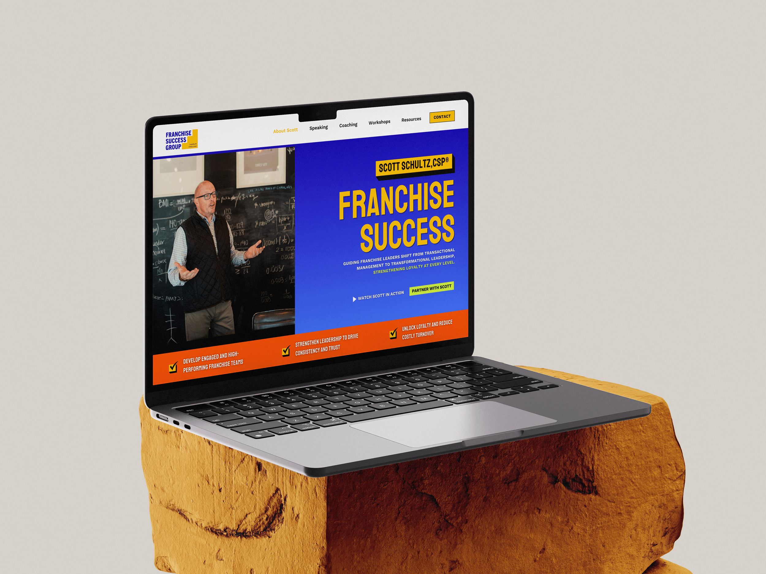 Open laptop displaying a website about franchise success, placed on a large orange rock. The website features a man speaking in front of a blackboard, with navigation menu and text about leadership and franchise development.