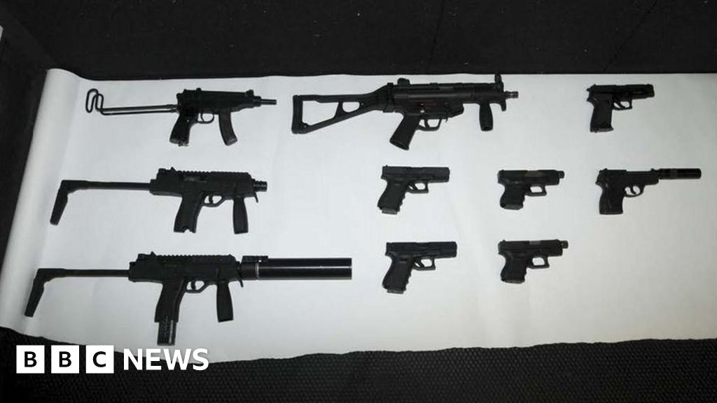 Multiple black toy or model guns laid out on a white surface, including rifles and handguns.