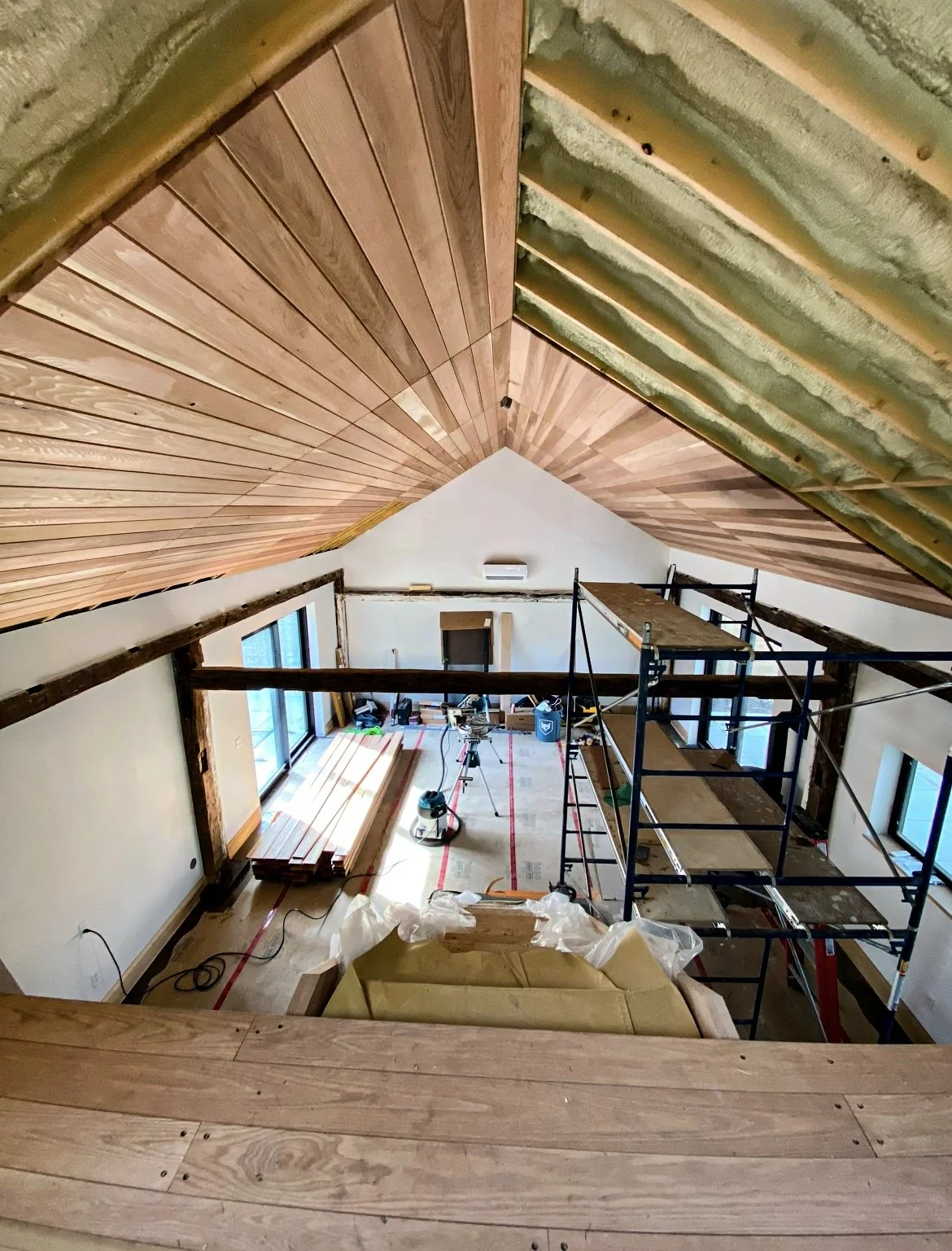 Interior view of a room under renovation with a vaulted ceiling, wooden paneling, scaffolding, and construction tools and materials.