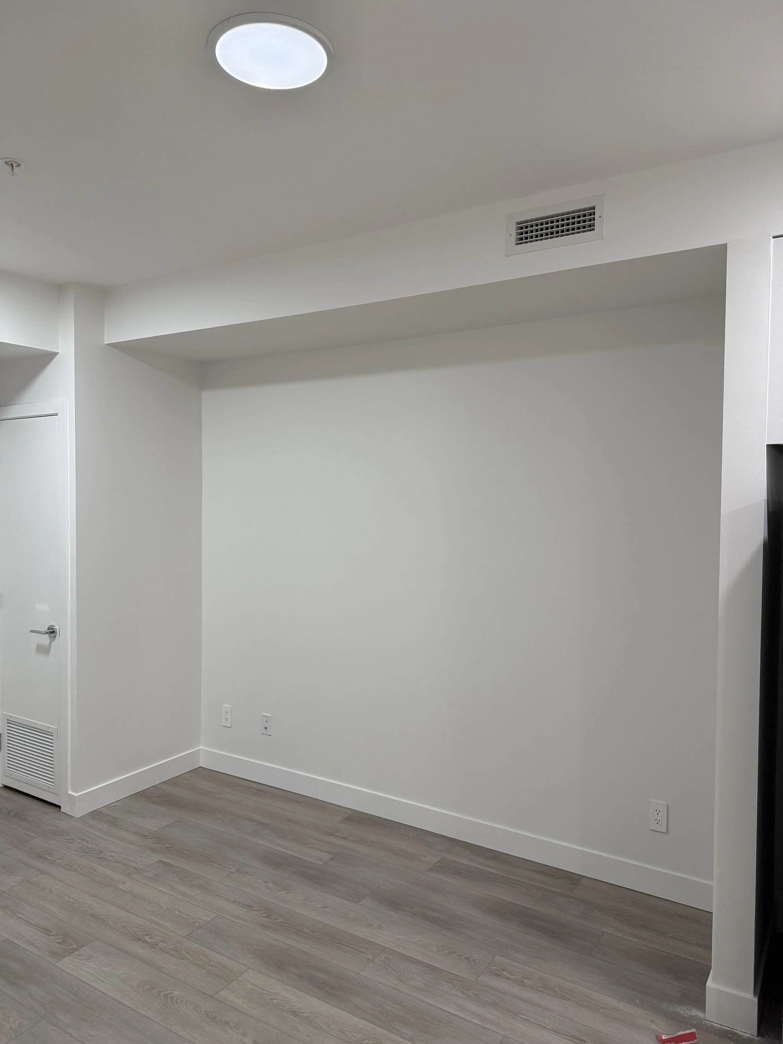 Empty room with white walls, light wood flooring, and a ceiling light fixture.