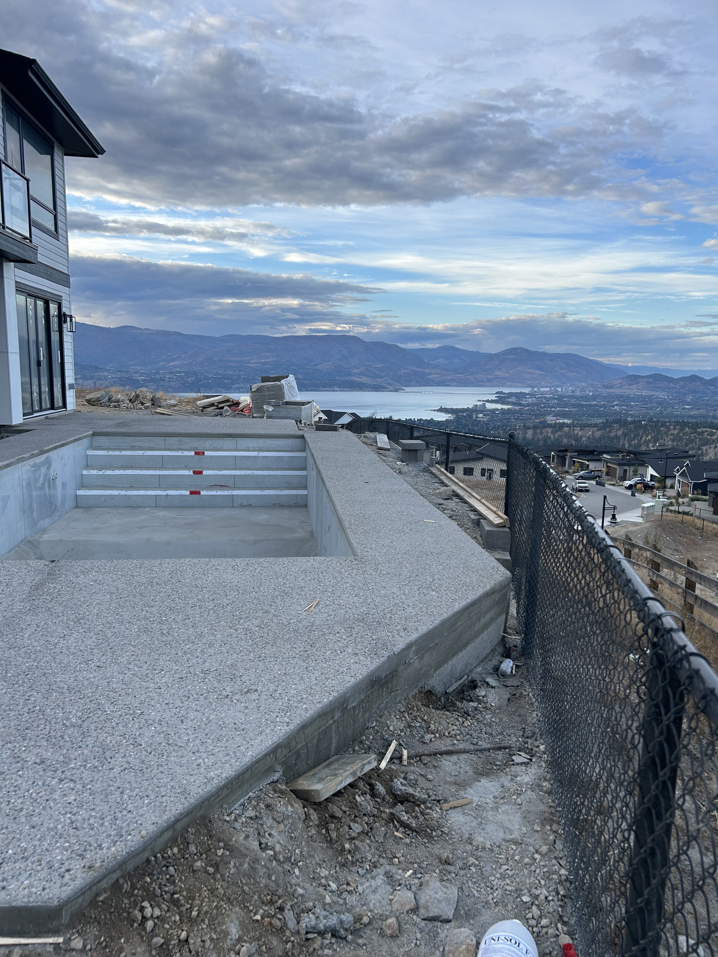Construction site with an unfinished pool, concrete steps, and a view of a lake and mountains in the background.