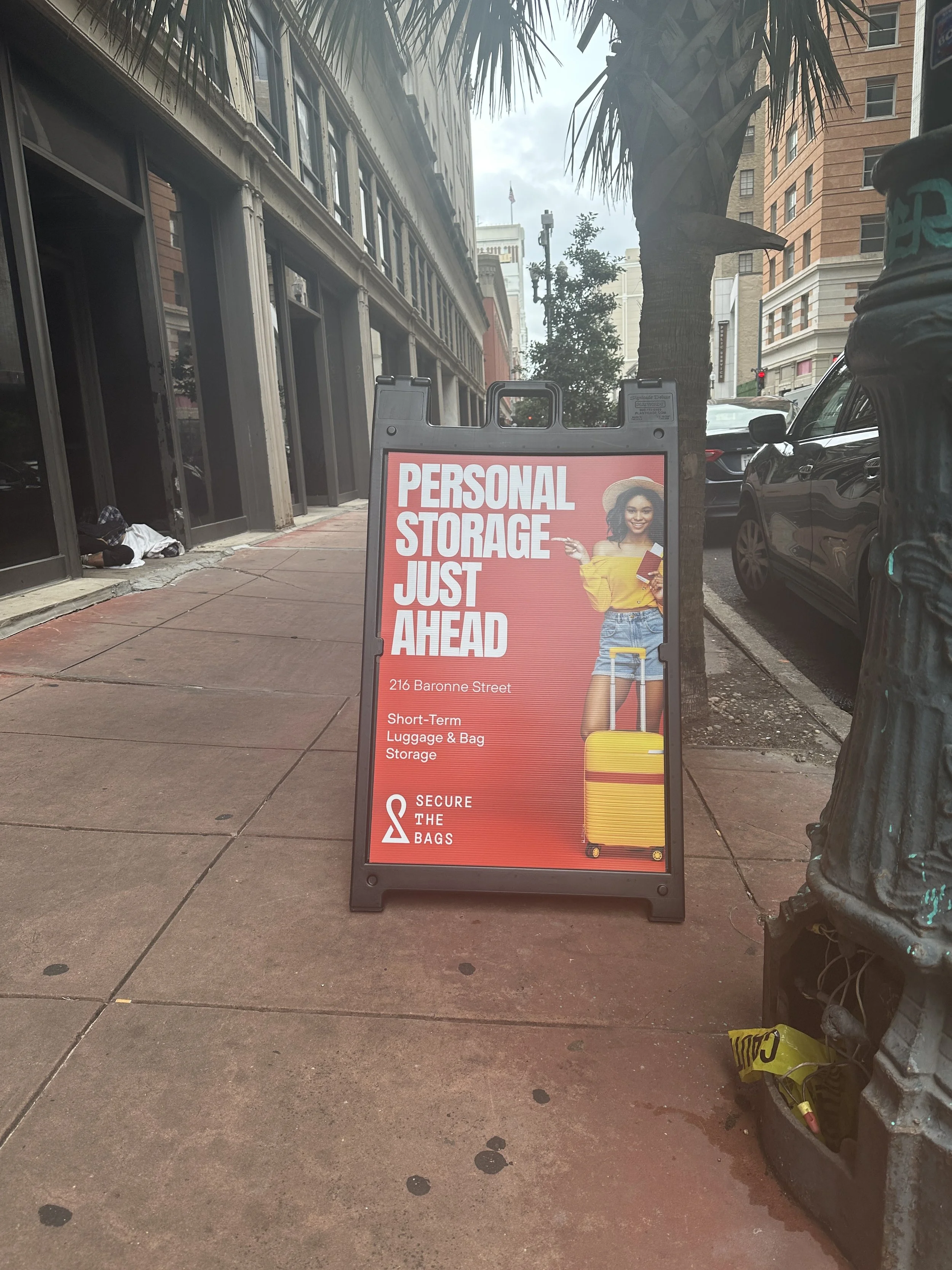 Sign advertising personal storage services at 216 Baronne Street, featuring a woman with a yellow suitcase and text promoting short-term luggage and bag storage.