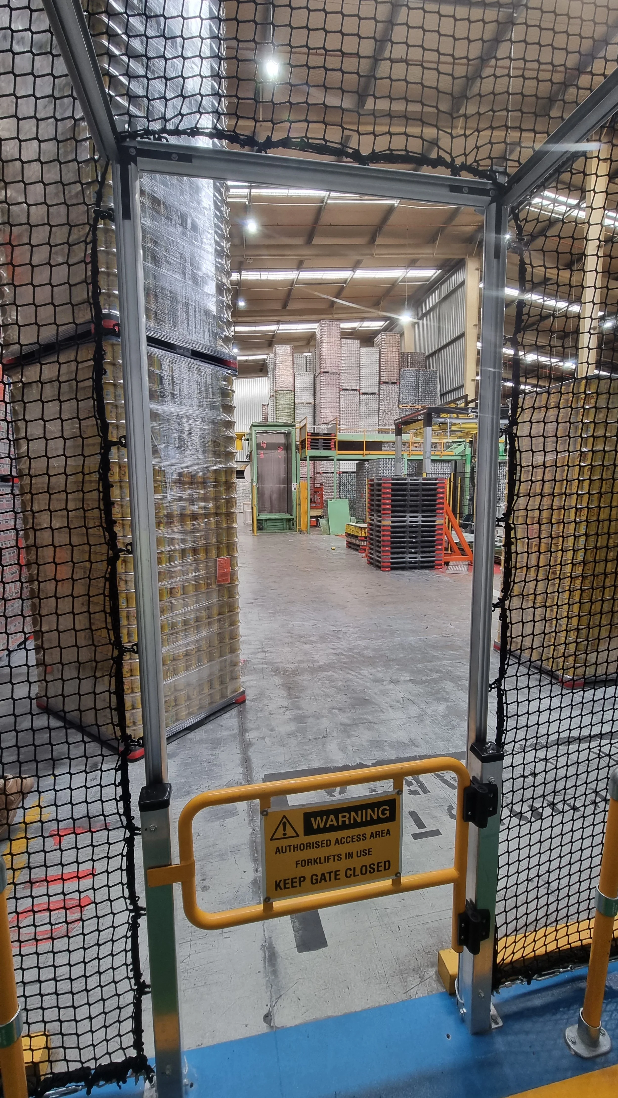 Warehouse with stacked pallets and a forklift zone with a safety gate and warning sign.