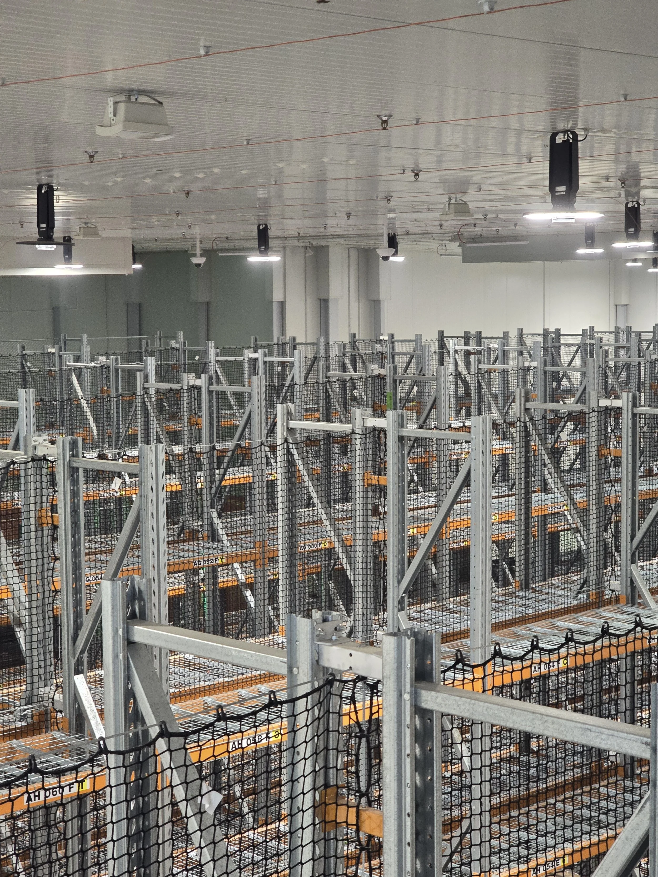 Empty industrial storage racks with metal frames and safety nets in a warehouse setting.
