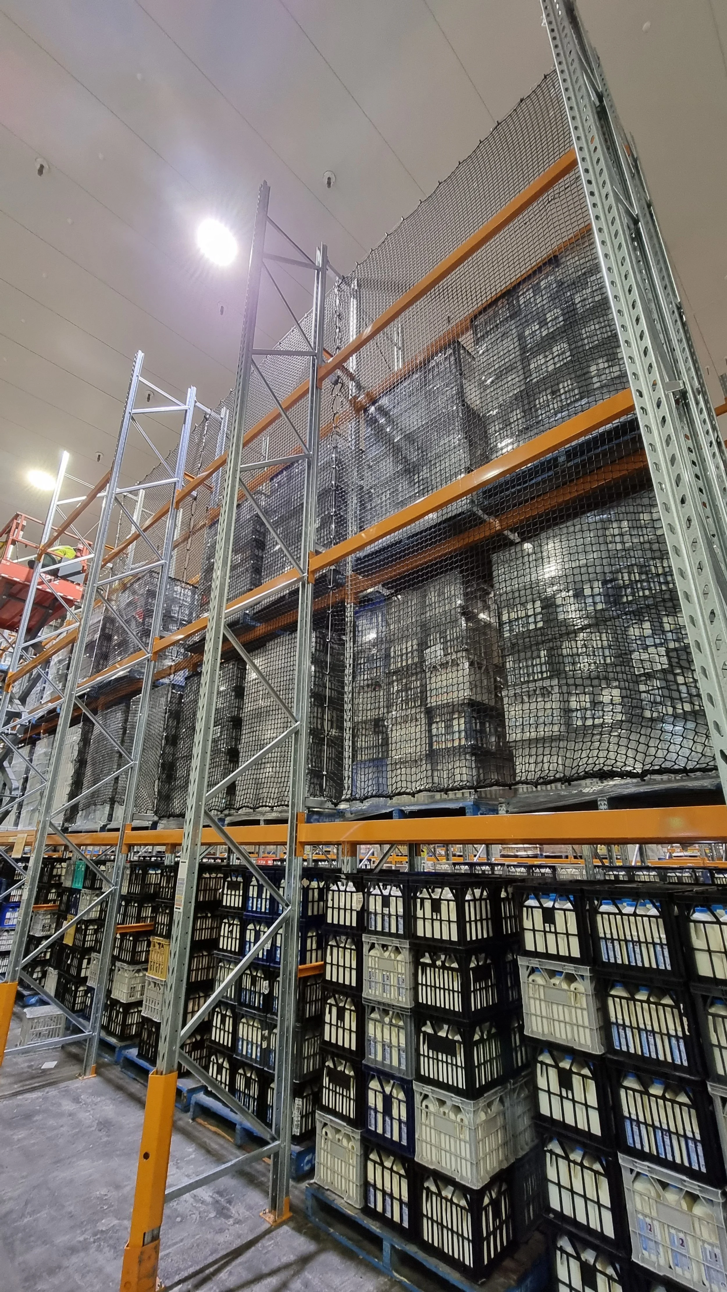 Industrial warehouse warehouse shelving with stacked crates and pallets, storage cages, and a worker on a scissor lift.
