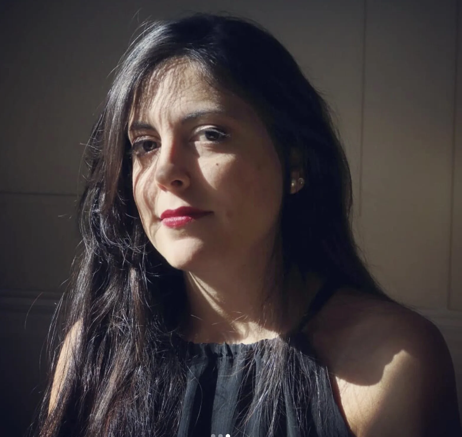 A woman with long dark hair and red lipstick looking slightly to her right in a dimly lit environment.