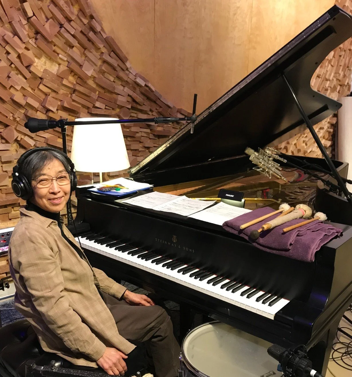 A woman sitting at a grand piano in a recording studio with soundproof walls, wearing headphones and smiling.