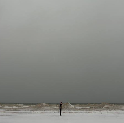 A person standing alone on a beach with dark, cloudy sky and choppy ocean waves.