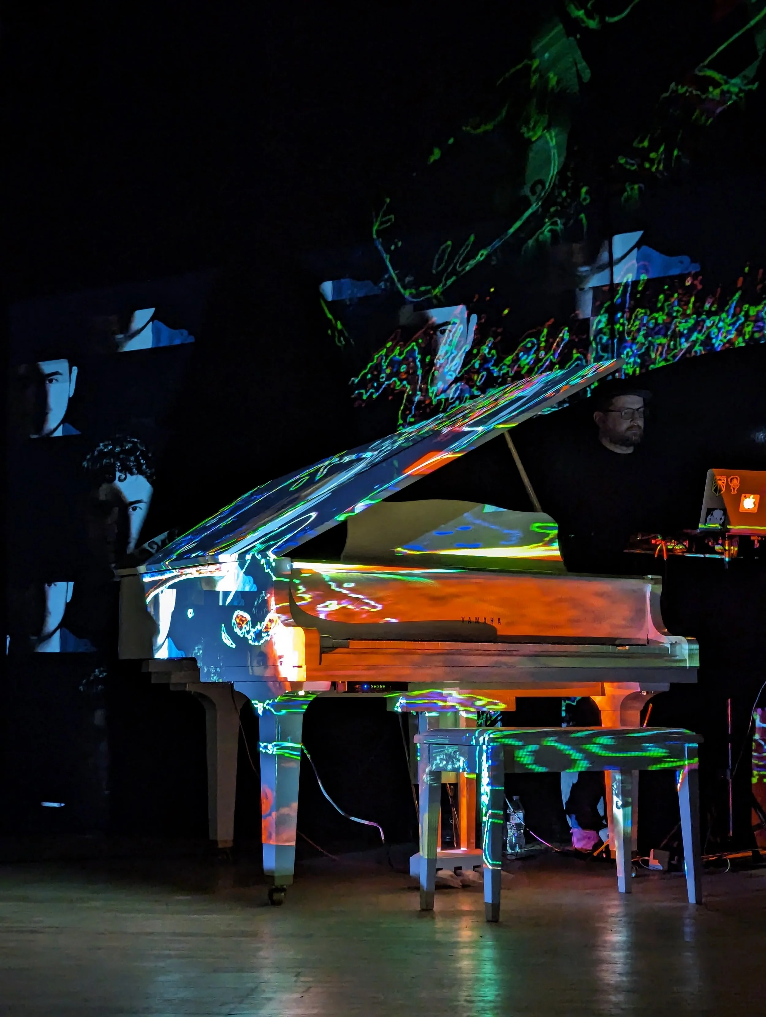 A white grand piano with colorful neon lights reflecting on its surface, set in a dark room, with people in the background.