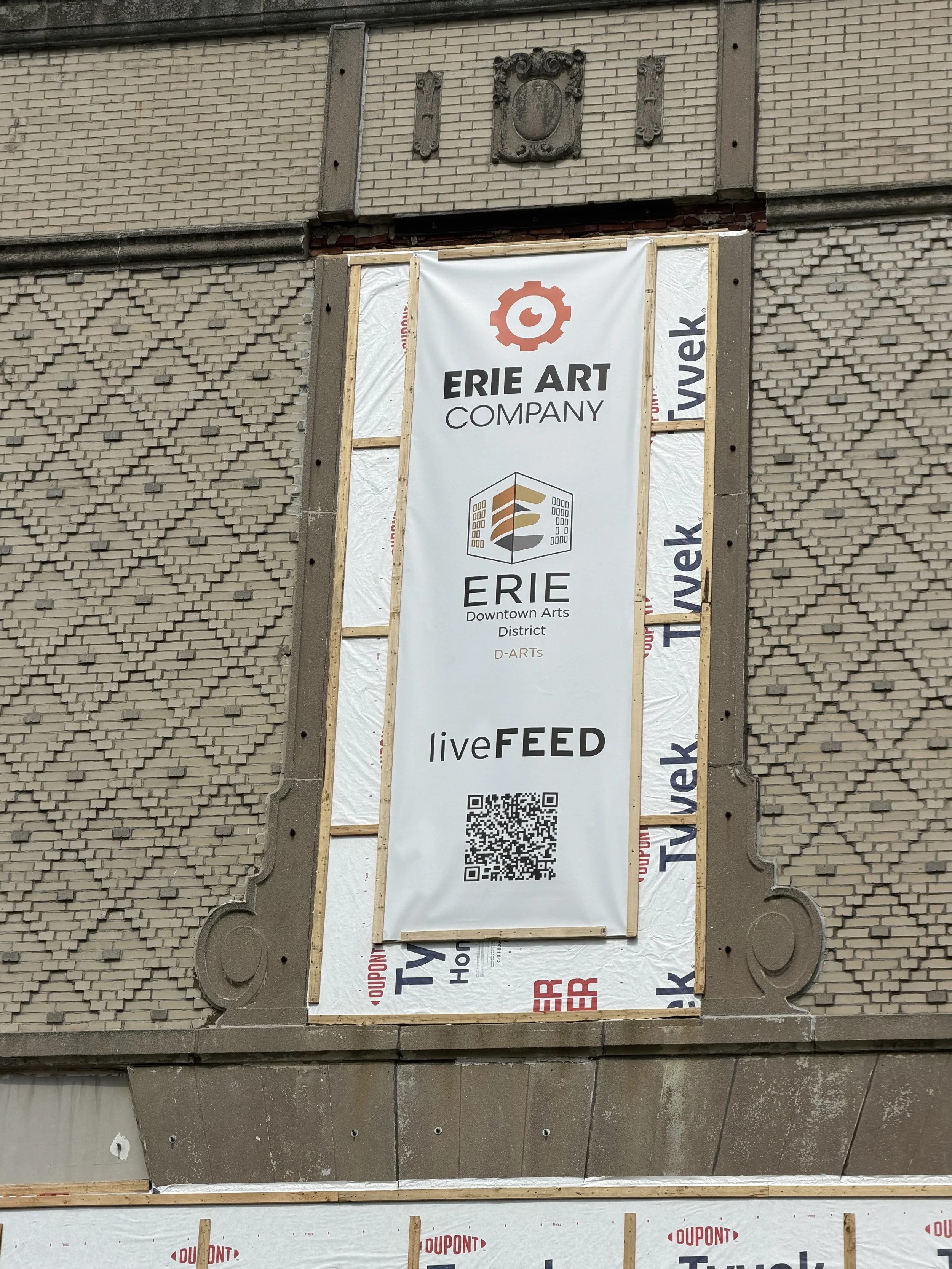 Sign for Erie Art Company and Erie Downtown Arts District, with a QR code, mounted on a brick building under construction or renovation.