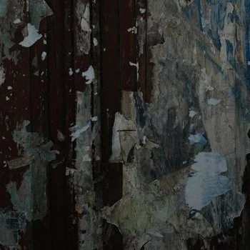Close-up of a weathered and chipped wall with peeling paint and exposed wood.