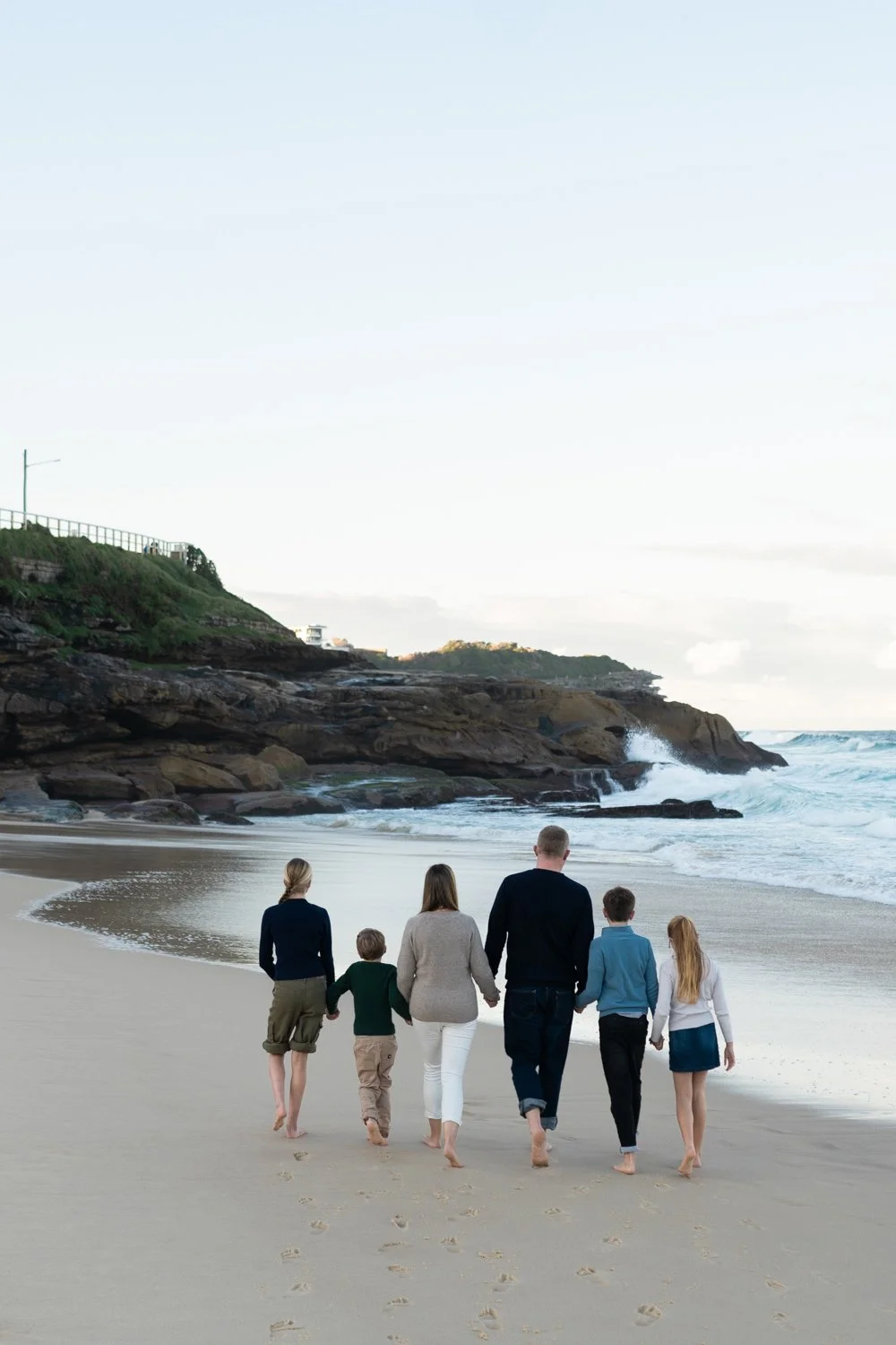 A family of 6 walking along Bronte beach at sunset, waves rolling beside the rocky shoreline