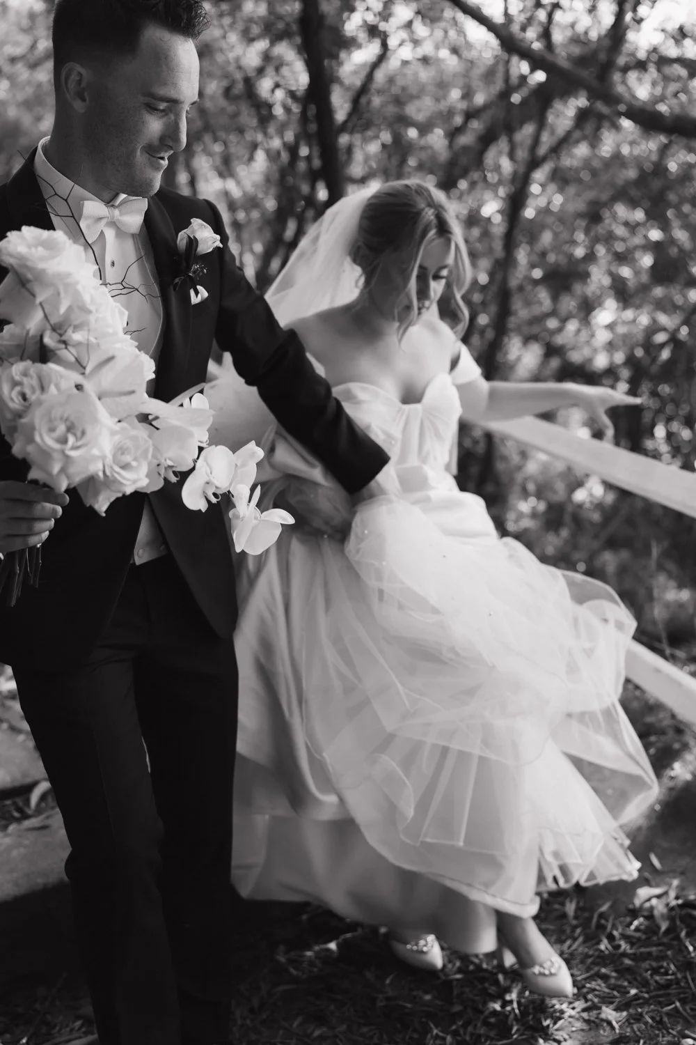 Black and white candid moment of groom helping bride step on trail.