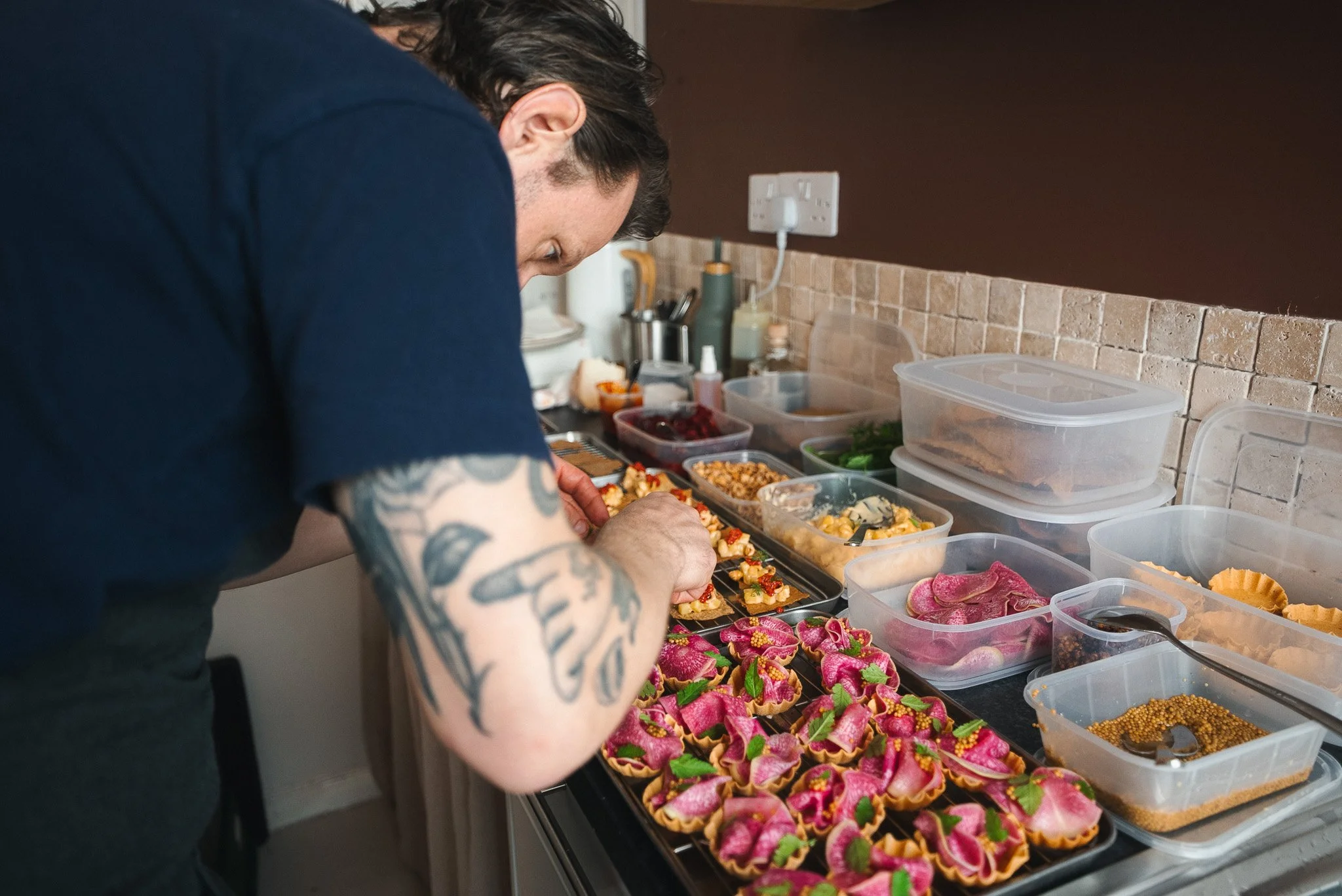 A chef preparing colourful canapés on a kitchen counter for a launch party event.