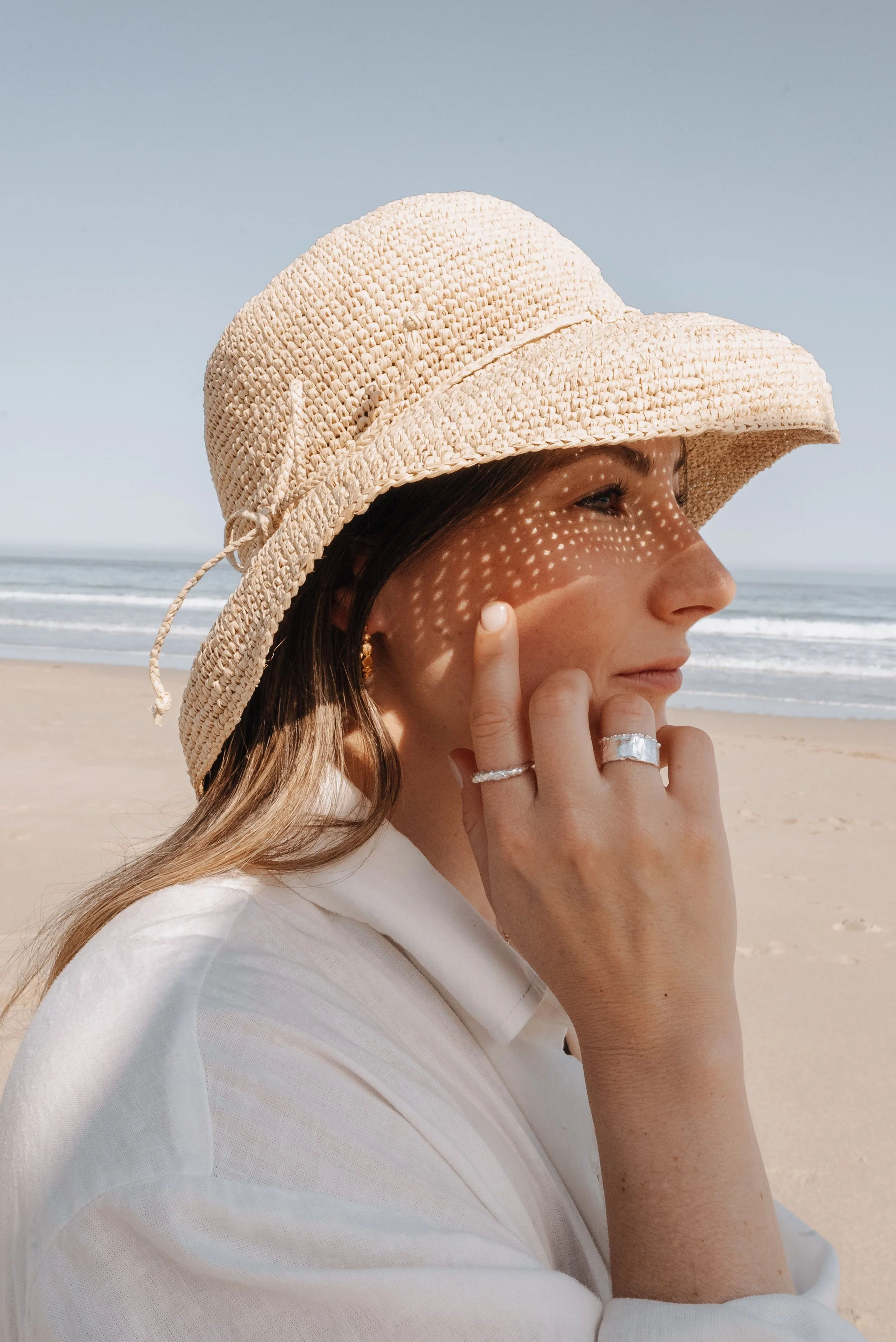 Woman wearing a woven straw sun hat showing layered silver rings and a gold hoop earring