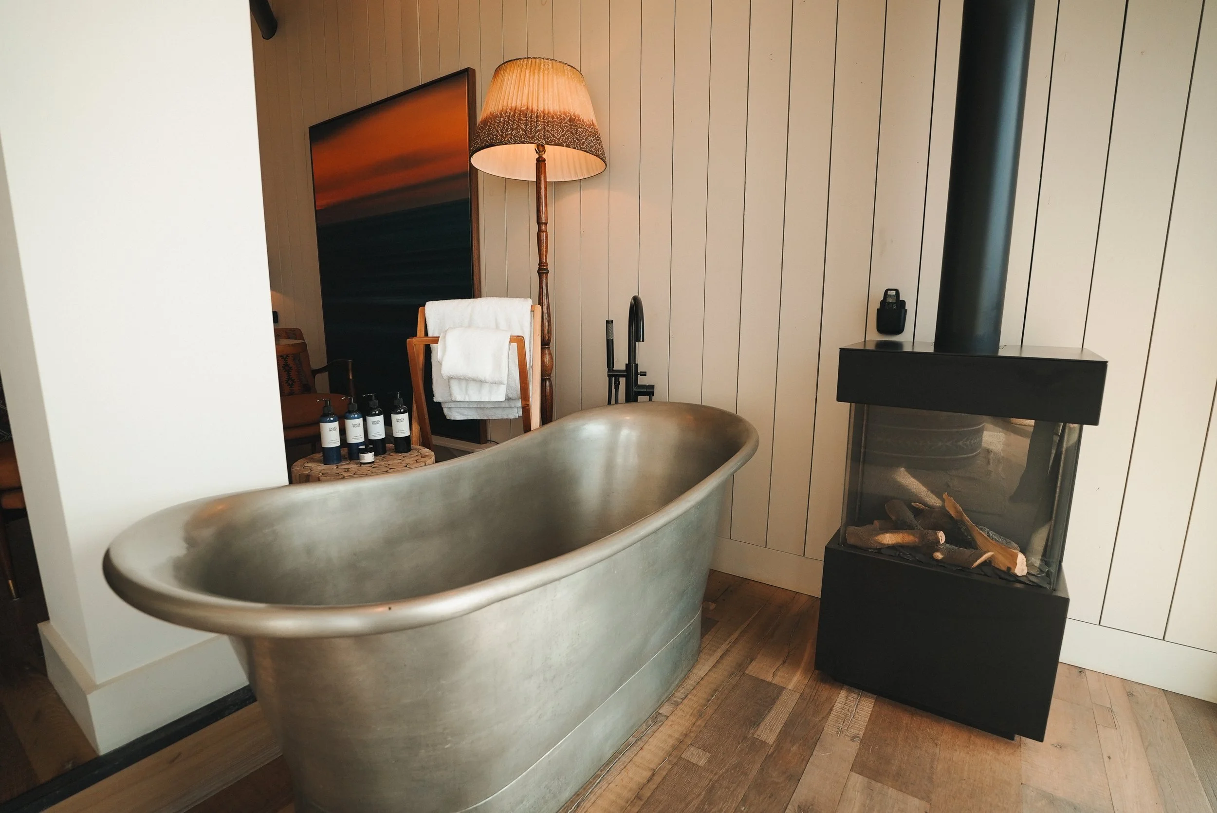 A luxurious hotel room with a bathtub and a modern black log fireplace.