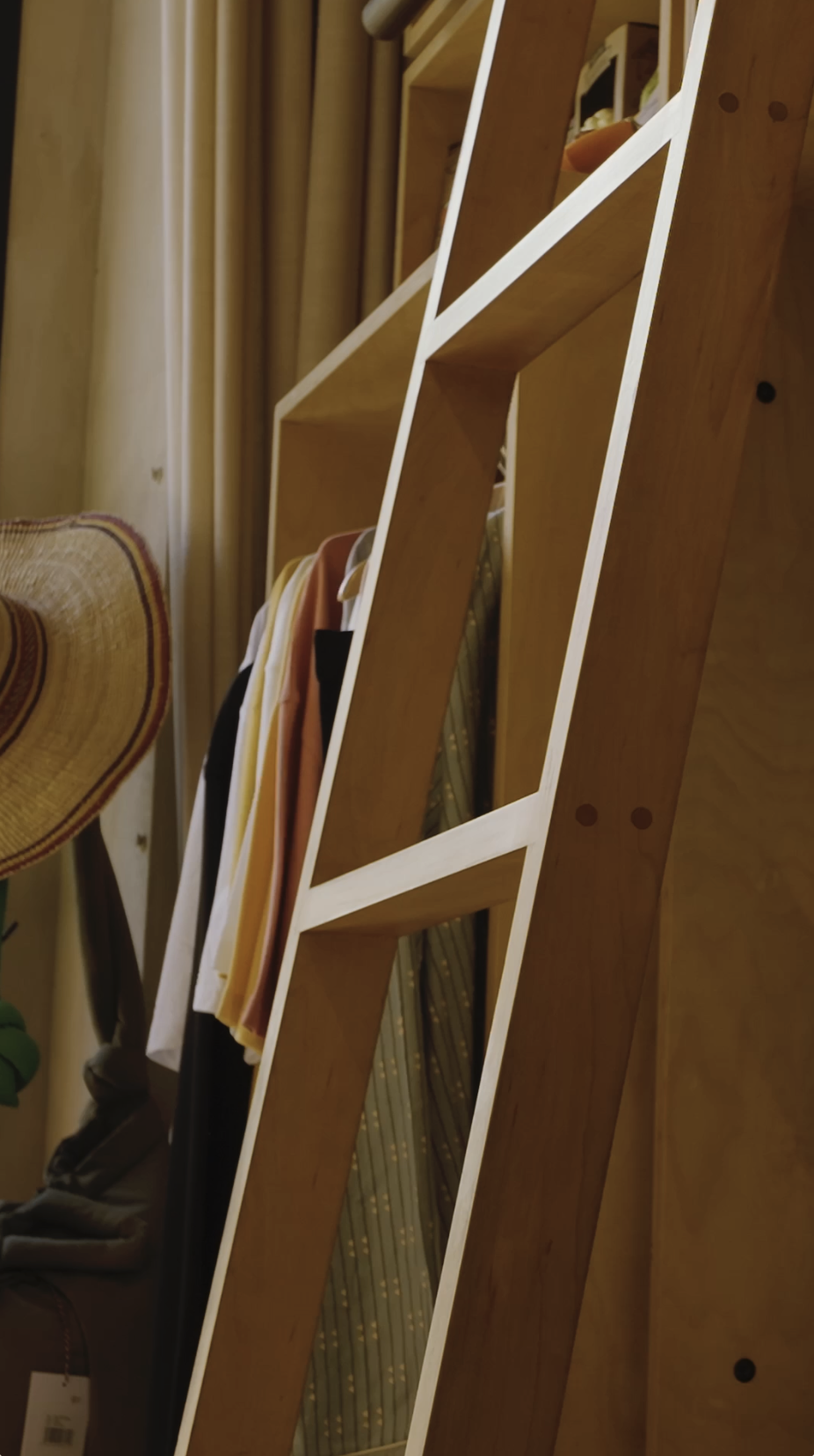 A hotel boutique shop, wooden shelving unit with clothing and a hat, positioned indoors with curtains in the background.