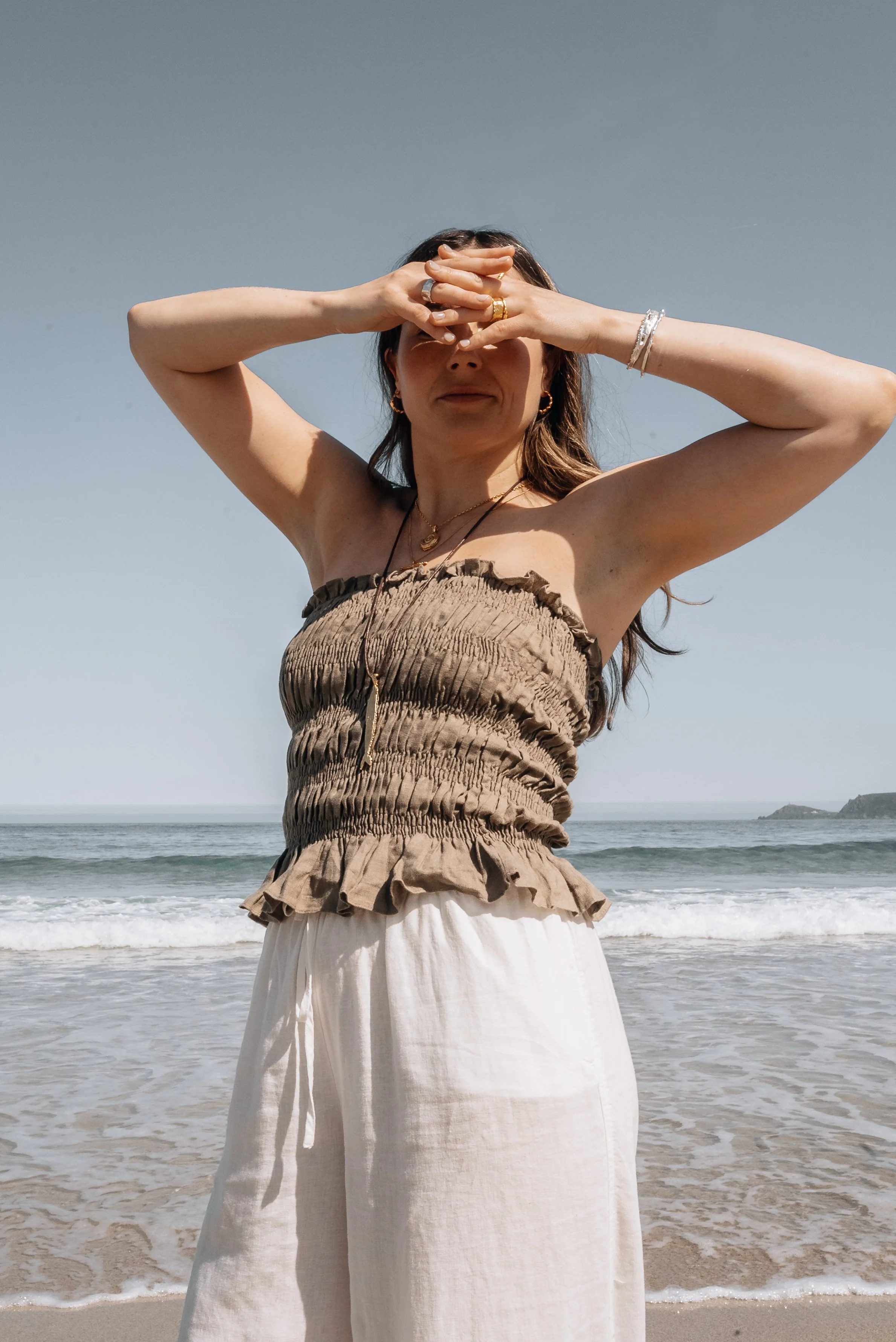 Woman on the beach wearing layered gold necklaces, rings and a silver bangle