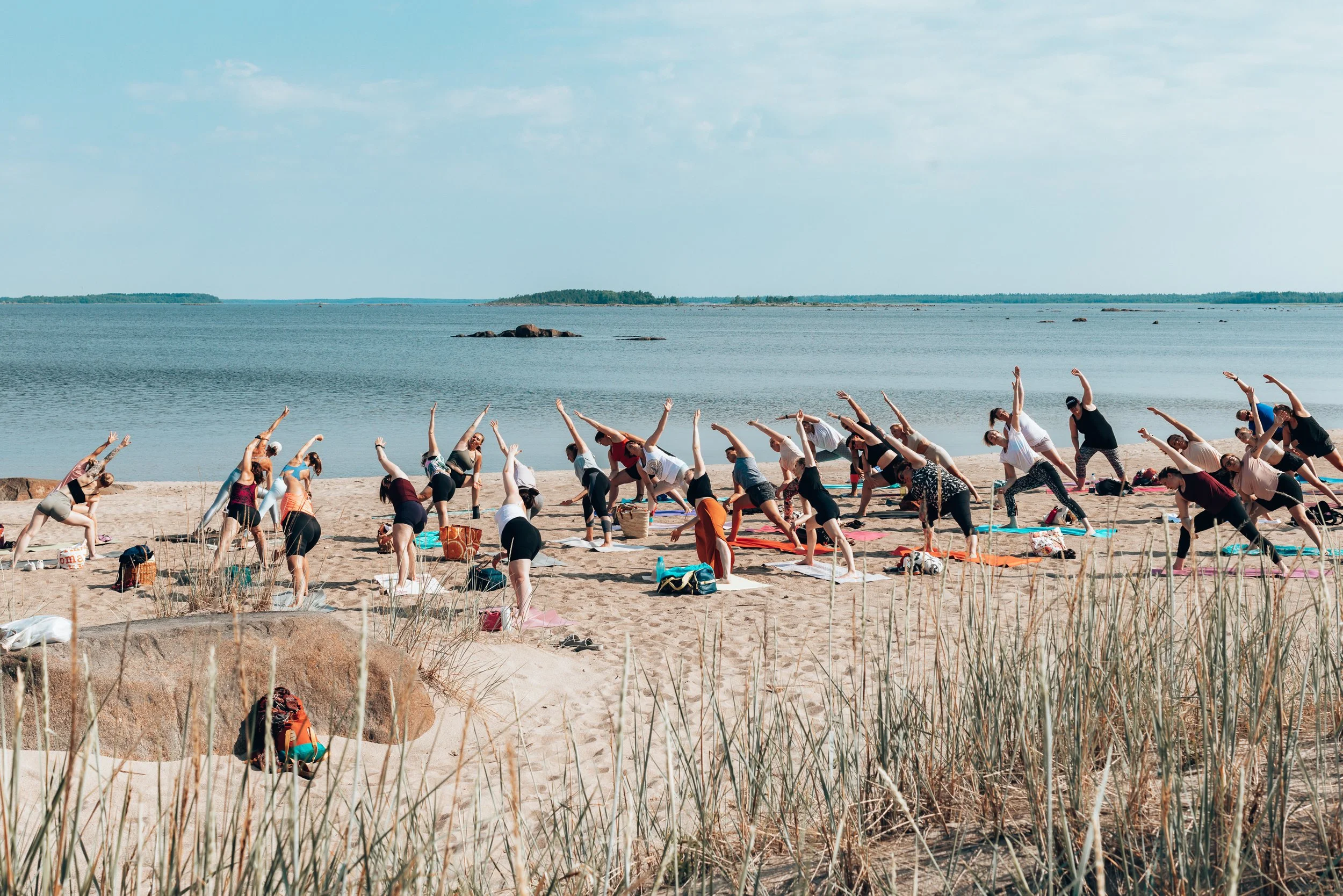 Group of people doing yoga on a sandy beach near water during daytime.