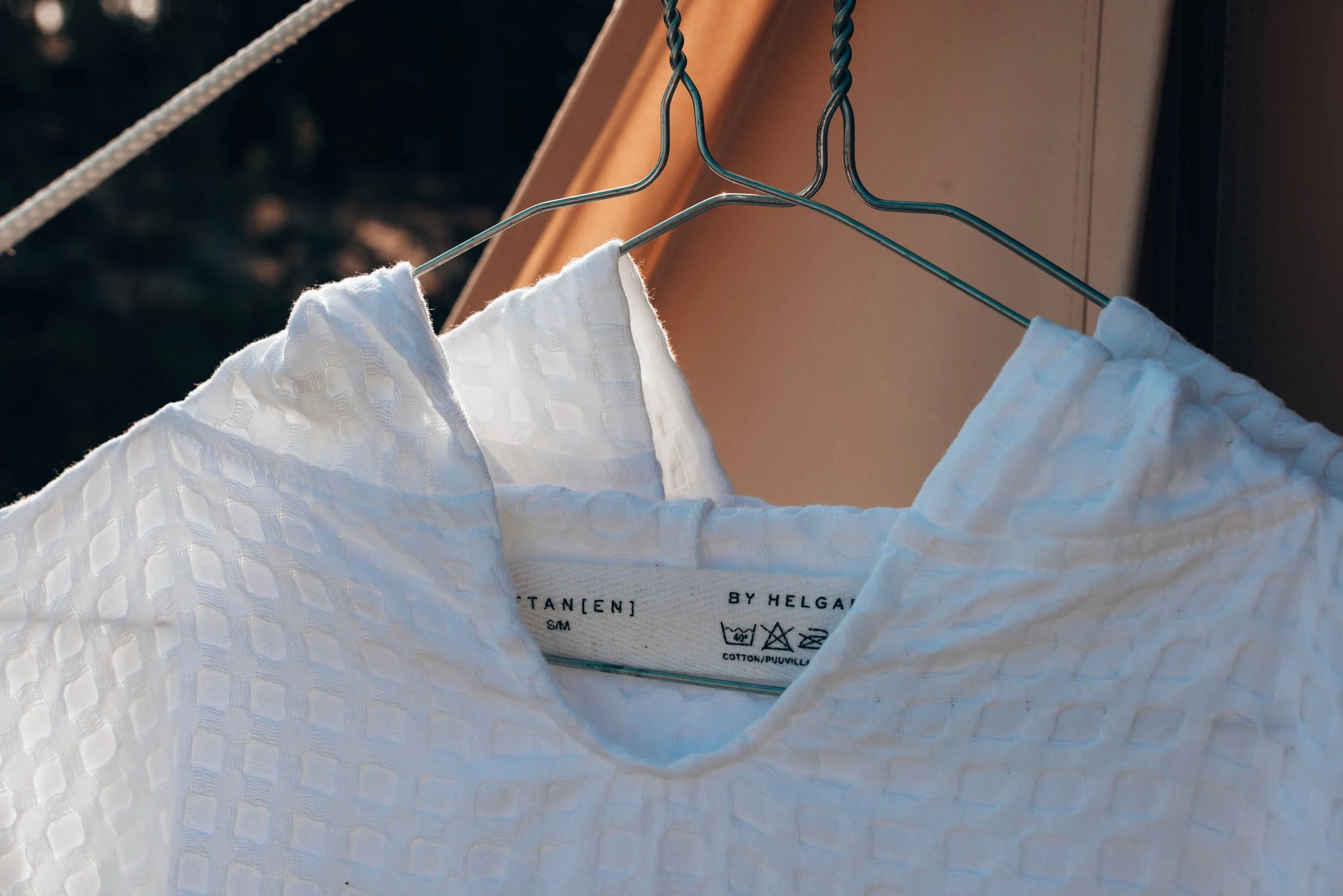 White textured fabric hanging on a wire hanger outdoors, with sunlight illuminating it.