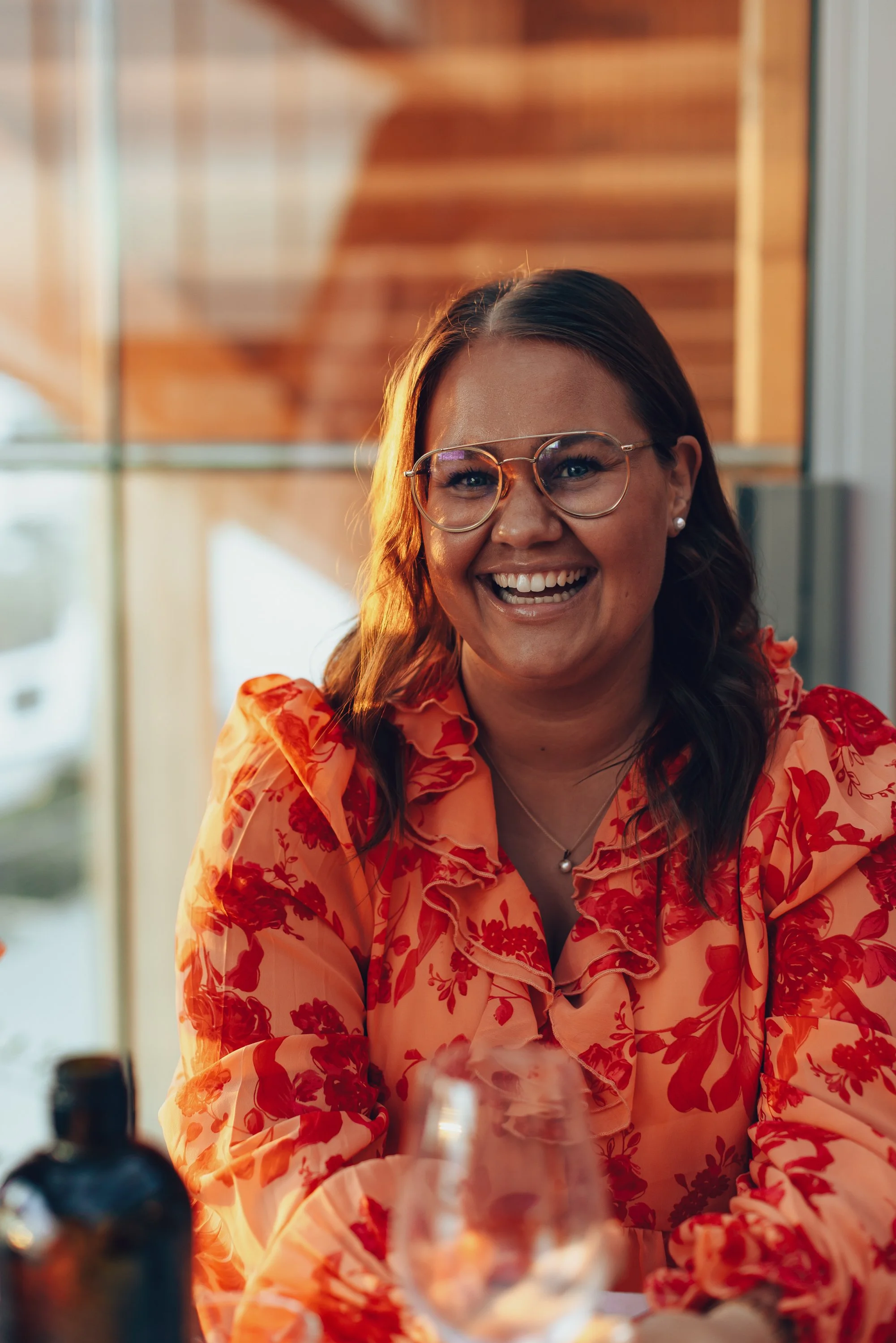 A smiling woman wearing glasses and a floral orange blouse sitting at a table.